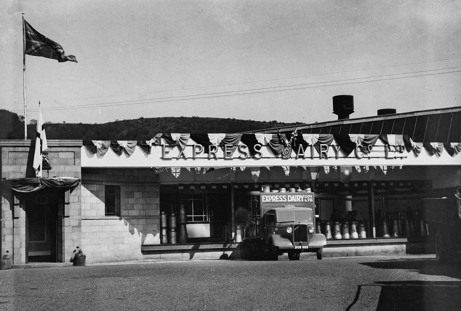 1933 Rowsley Dairy churn bank, decorated with bunting, with churn truck Co. No: 190, Reg: BGW 868. Bill Conquest suggests "Possible royal visit". (Courtesy Derbyshire Record Office, donated in March 1985; they had previously belonged to the donor's father, who was an electrical engineer with the dairy.)