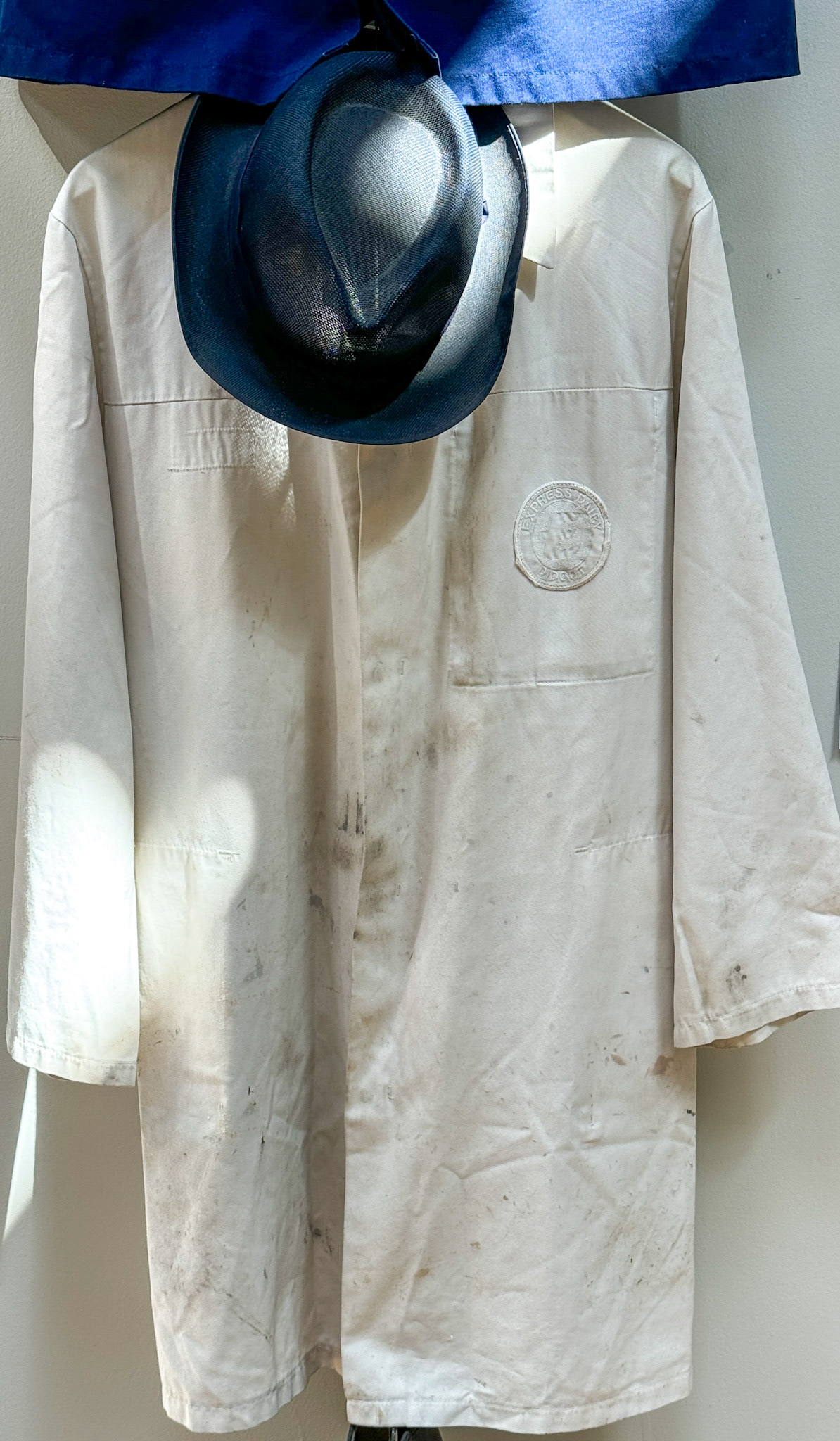 2025 White lab coat and blue trilby, worn by supervisors and managers at the dairy. (Didcot Dairy Exhibition 2024, Cornerstone Arts Centre)