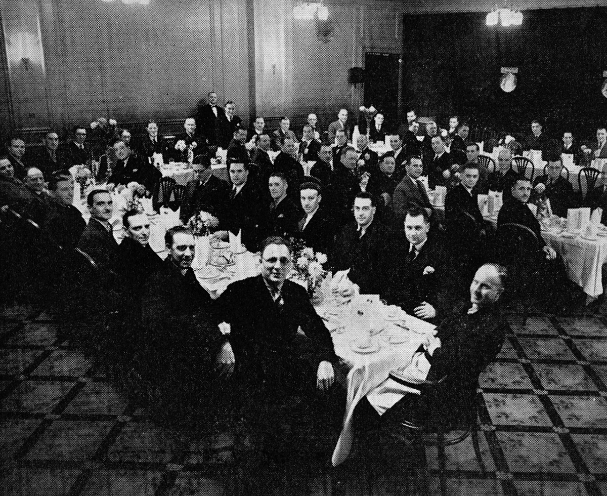1934 West London Managers' dinner at the Clarendon Hotel, Hammersmith. At the top table, those still serving are grouped conveniently together... Mr Walter Nell, Mr W. E. D. Bell (standing), Mr W. E. Farmer and Mr G. R. Gervis. Among those no longer with us are Mr Dean, Mr D. M. Galbraith, Mr A. E. Rumbold, Mr T. D. Tyler, Sir William Manchester and Mr A. Whittaker. At the near table, turning to face the camera, are Mr S. A. Marshall and Mr R. Brame. On the far side: the two Donovan brothers and Mr A. Burrows. At the centre table, you can spot Mr R. W. Lovett, Mr J. W. Duncan, Mr J. W. Esling and Mr C. S. Kirby. (1960 Picture Set from Express News Christmas edition)