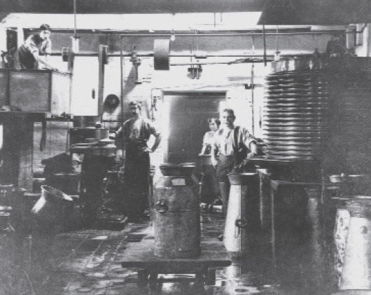 1920c Interior of Horner's Creamery. The dark man to the left is possibly George Homer with his wife, Ada, in the background. Charlie Haspell is the figure to the right with his left hand placed on a milk cooler and aerator-prior to refrigeration this was a common way to cool milk and remove odours-water, piped from Cuddington Brook, was used in the process. George Horner was advanced in his use of the commercial cooler and aerator which was the best of its type at the time. Only patented in 1908 it would have been shipped from the United States at great expense to Homer's, though in the long run it reaped rich rewards. From 'William Horner and His Creamery' by Jill King 2012