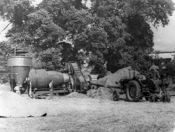 1950's Joel Street Farm, Northwood, Middlesex. The originator of the image, who lived on the farm as a boy, said “Perhaps someone can identify this next machine, which seems to have cone separators. It might have been something to do with oilseed production, Dad did talk about them doing that during the war”. Rural Museum Network members commented "...could be a small seed thresher (flax / clover)-I have a clover thresher by Hunts of Earls Colne that uses a similar drum type separator" (Neil Syrett), "The tractor is a Fordson E27N Major which was introduced in 1945 (and replaced in 1952), so the picture is post 1945" (Thomas Jackson), "The tractor is a Fordson E27N Major, which was in production from 1945-51. This one has electrics so would be post ’46. Best guess on the apparatus is for grass processing, probably for seed." (Stuart Gibbard). (Photo courtesy John Stonehill)