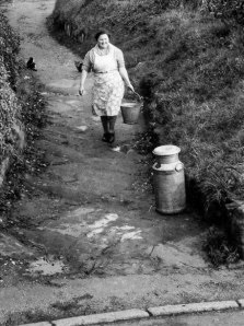 1950's drinking water to the cottages, to be stored in redundant milk churns, but rainwater had to be collected for other uses. The lady coming up Woodview Lane on the Brownhill to get her pail of water was Mrs. Maud Fox. (Courtesy Yoland Brown)