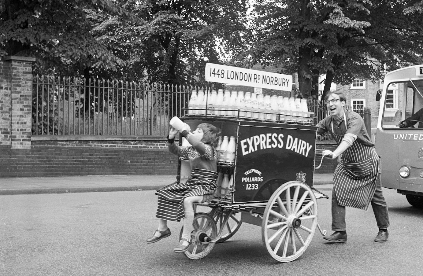 1969 Express hand cart being pushed along the road in front of a United Dairies float as part of a parade passing along South Grove during Highgate's 'Fair in the Square', an annual event held in Pond Square. (Historic England Archive)