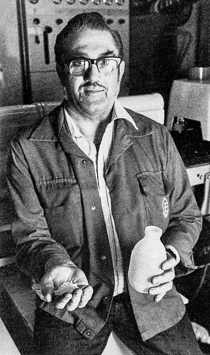 1984 Les Hays, chargehand in the blow moulding area, with a handful of granules — 18g to be precise—which is all that is required to make the bottle he is holding in the other hand. Les, who has been with Express Dairy for eight years, works a 12-hour day shift, from 8 am to 8 pm. The blow moulders work around the clock; the raw plastic being fed into them from a 40 tonne silo. They gobble up two tonnes of granules each day, and produce 120,000 bottles. The new blow moulder will greatly increase that output. The bottles, once made, are blown by compressed air along tubes to the bottle fillers. Most of his colleagues wear ear protectors. Les's solution to the noise problem, caused by the grinders, is cotton wool, because he finds it much more comfortable. Away from his job, Les — a married man with a son, 19, and daughter, 22 — 1ikes to visit places of interest and take photographs. His face may look familiar to wrestling fans, he used to wrestle as an amateur and a professional in Bradford. He was a lightweight in those days, weighing in at nine stone 12 ounces. (Express News Spring)