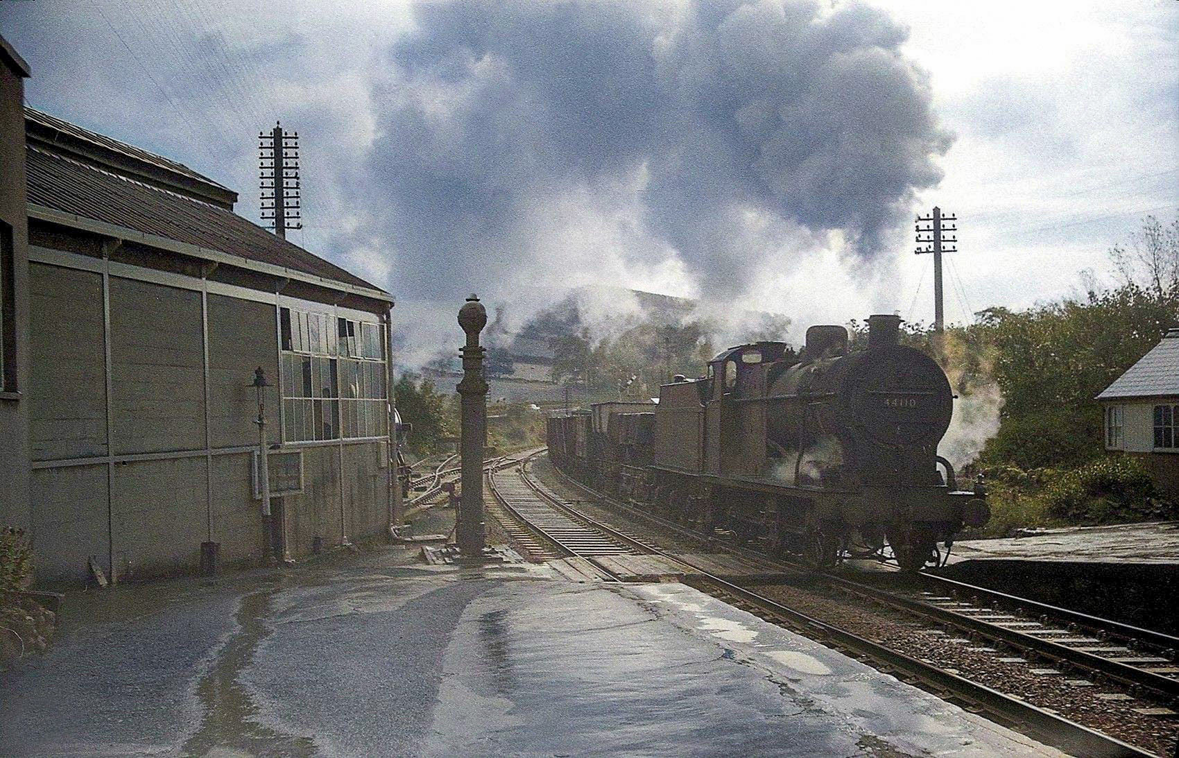1963 Rowsley station. Dave Winter comments "4F 44110 forges north with a freight through Rowsley station after a heavy shower on 5th October. A milk tanker is just visible peeping out of the Express Dairy building. 44110 was built at Crewe in 1925 with right hand drive, and was withdrawn six months after my photo was taken, being cut up in Rotherham. Five years later the line itself was scrapped. My original black and white photo has been 'colorised'. (Courtesy Dave Winter)