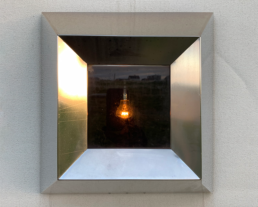 Stainless Steel Window with warm light bulb in the center through a canvas structure of Steilineset Minnested by Peter Zumthor in Vardø, Norway