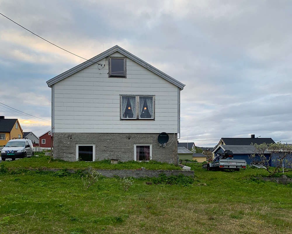 Home in Vardø, Norway with hanging lights in the windows and wide ship-lap siding