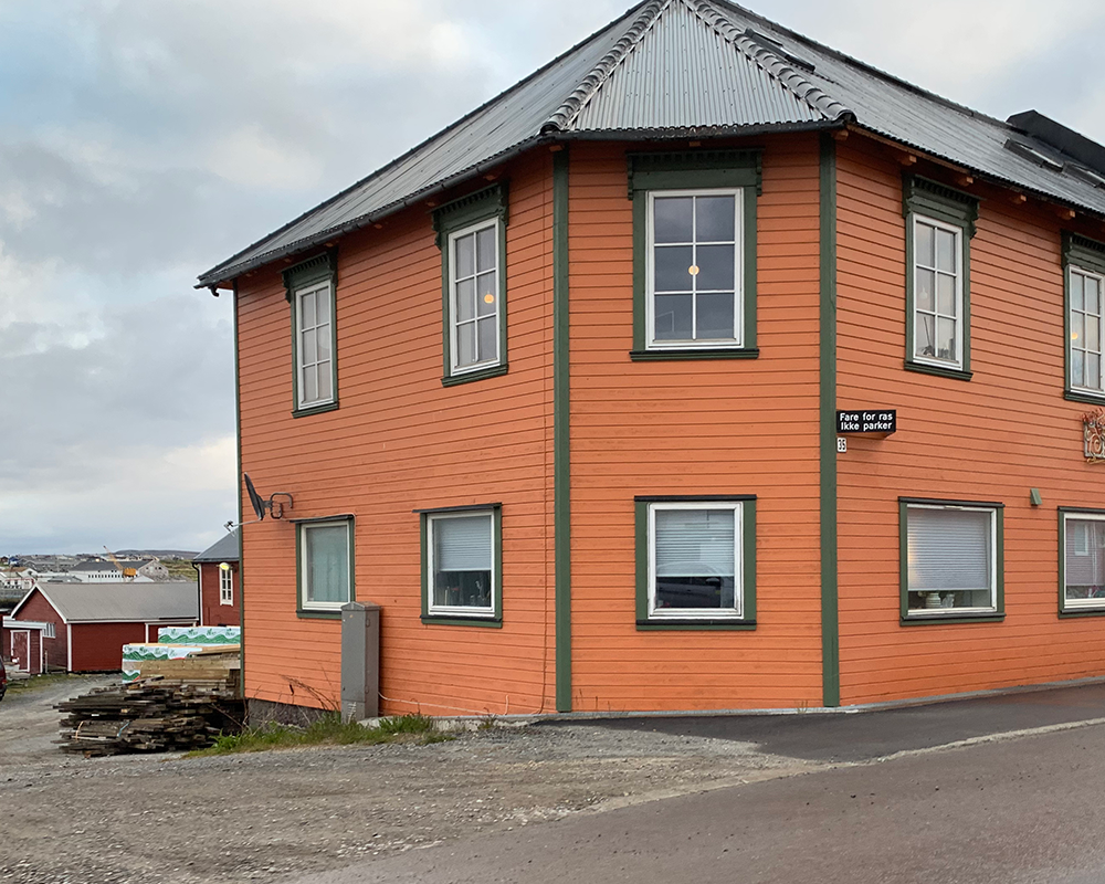 Orange House with green trim in Vardø, Norway with lights in the window