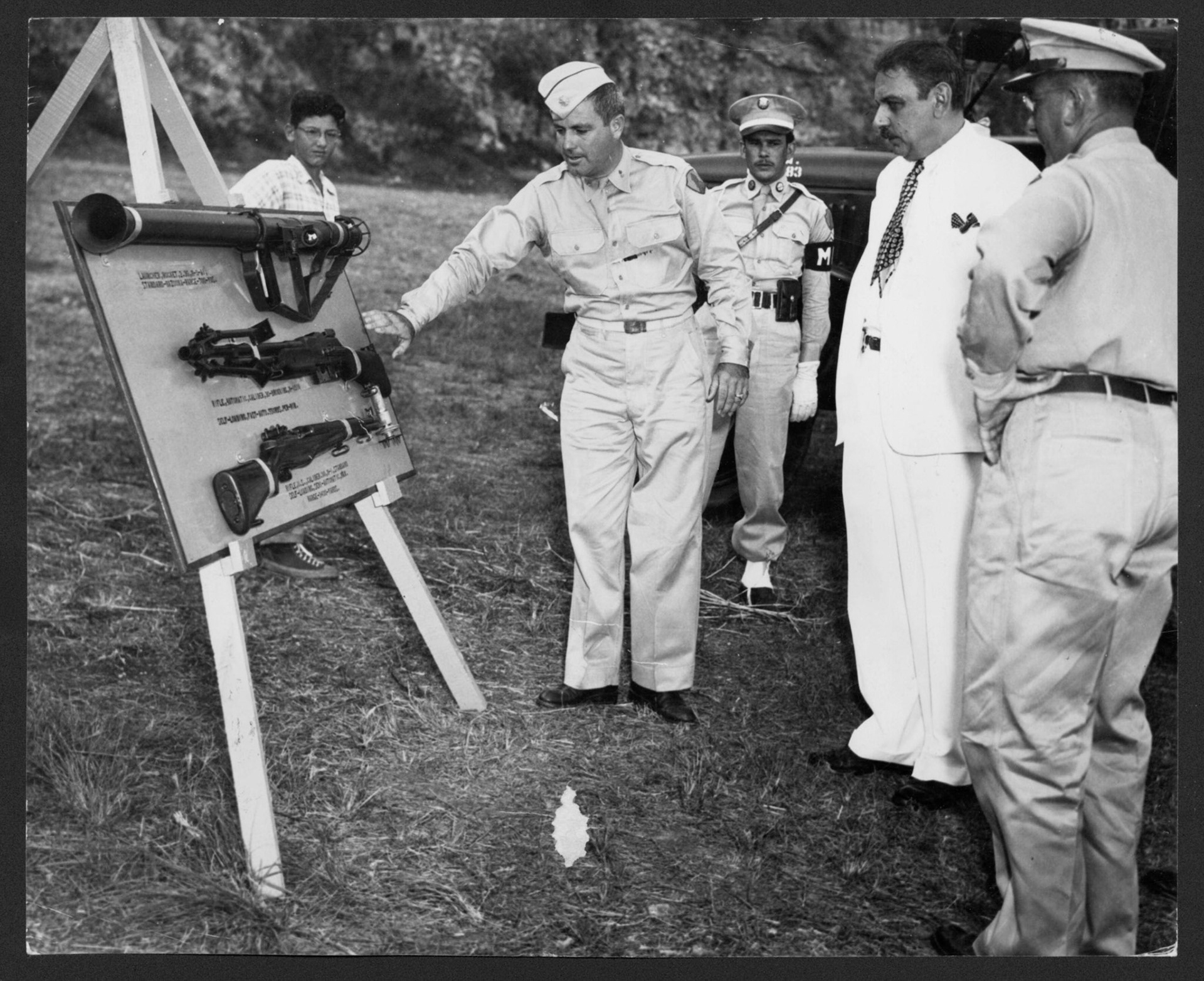 Oficial militar mostrándole al gobernador Muñoz Marín tres armas largas expuestas en un trípode.Fuerte Buchanan, Guaynabo.Abril 10, 1949