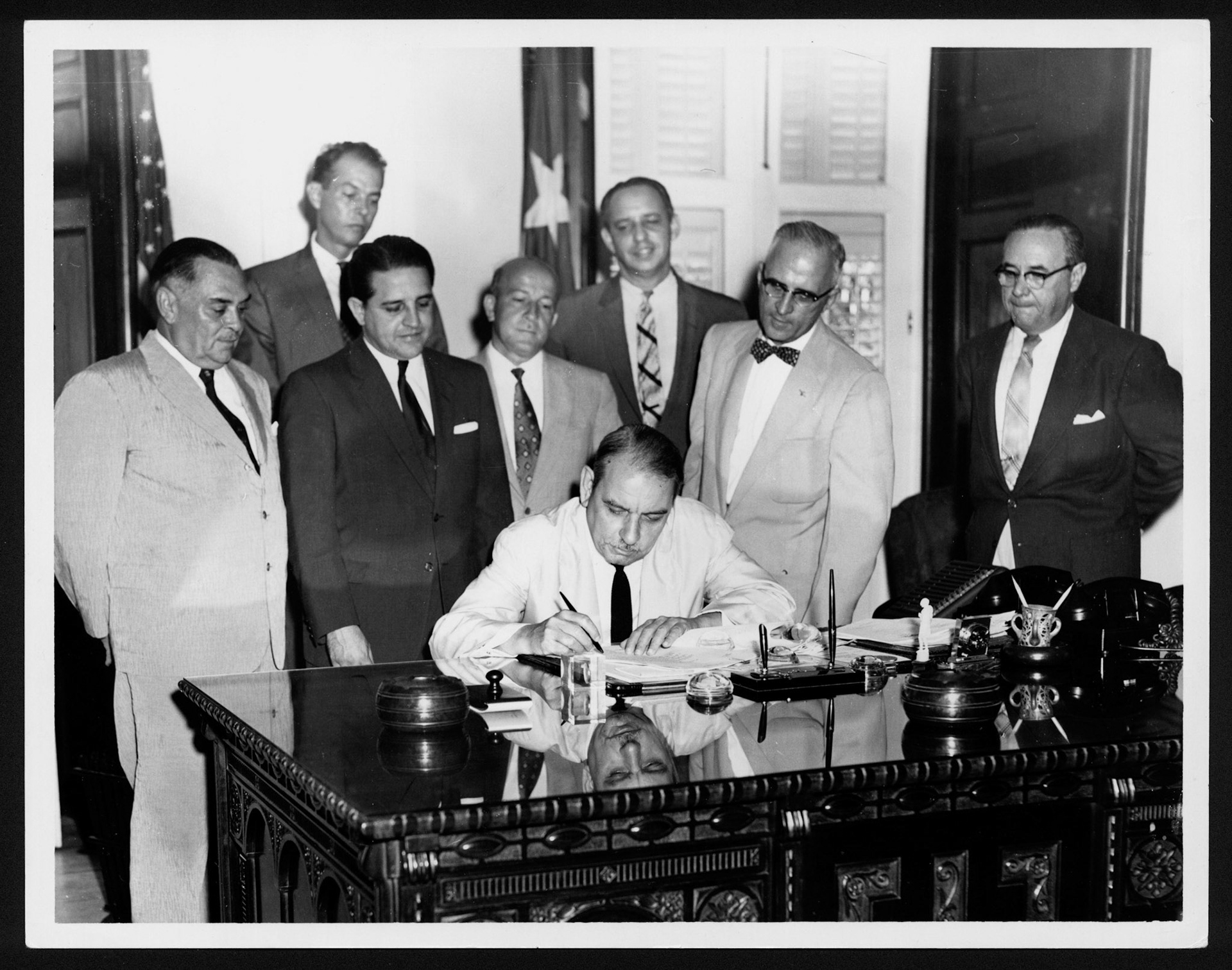 Gobernador Muñoz Marín firmando documento en su despacho mientras observa un grupo de médicos.La Fortaleza.1961