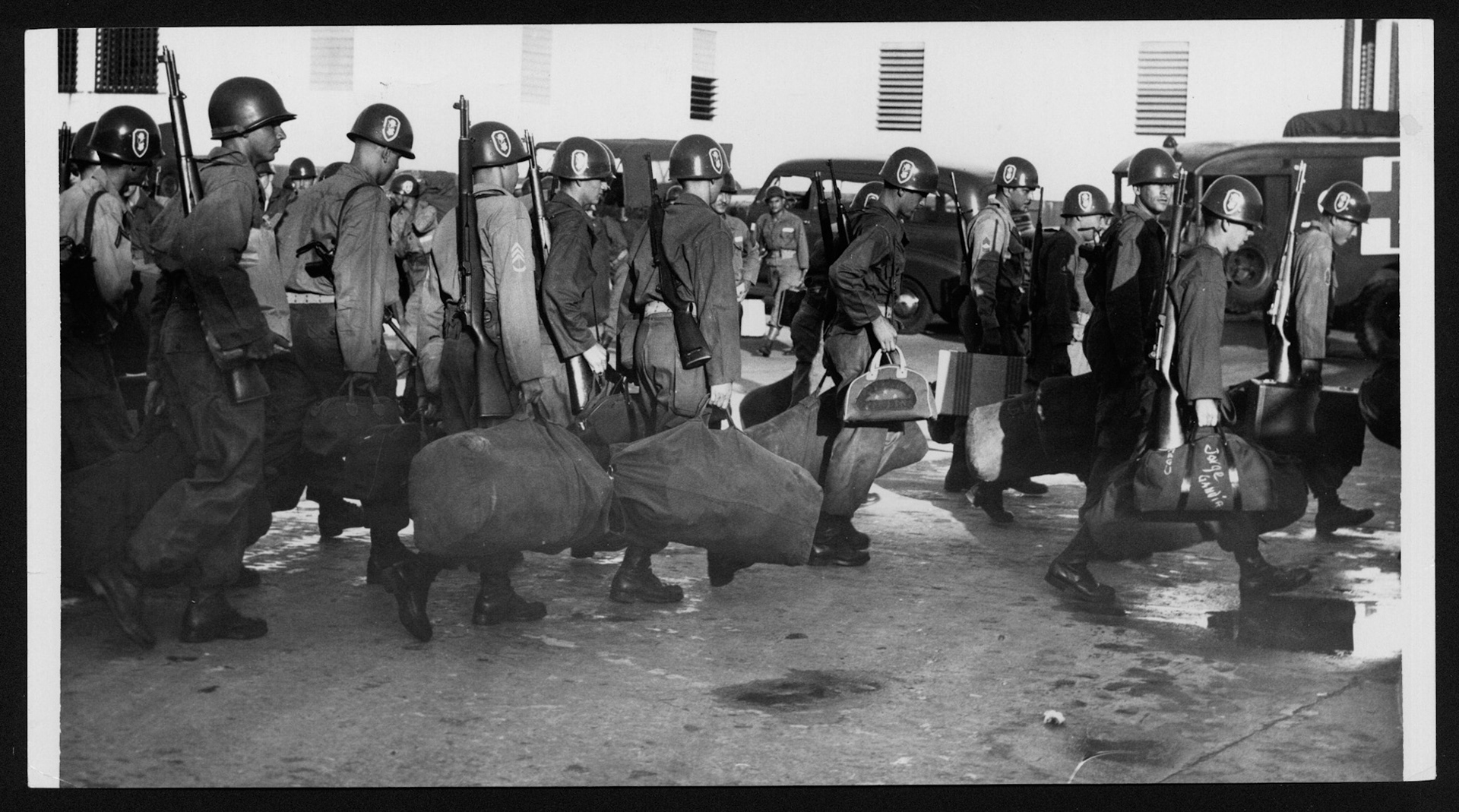 Militares caminando cargando con su equipo para ser transportados rumbo a campamento en Salinas.Julio 12, 1954