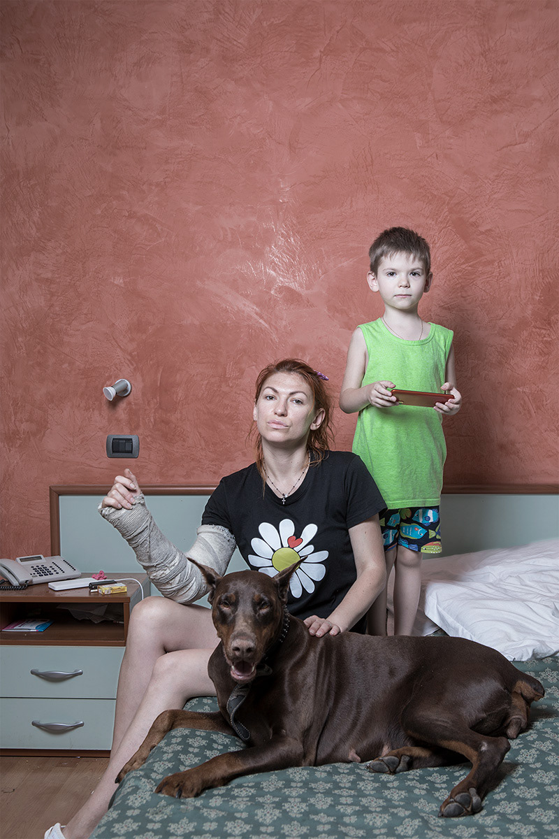 Frosinone, Italy – May 26, 2022. Lena Lisogor, from Kharkiv, is staying at the Astor Hotel in Frosinone with her son Egor and their dog Hana. She lived in the Severnaya Saltovka district, one of the first areas bombed. When the war began, she and her son spent 10 days in a damp bunker where children coughed constantly, and she still had to go outside under shelling to walk the dog. A friend helped them reach the chaotic train station in Kharkiv, where Lena boarded a train to Lviv without even knowing the destination. The journey was traumatic: the train was overcrowded, bathrooms were unusable, fights broke out, and she and her son stopped eating or drinking to avoid needing the toilet. After 20 hours they reached Lviv, where freezing temperatures, lost children and overpriced rooms made the situation desperate. Thanks to a friend’s tip, Lena found temporary shelter in an office until March 10, when bombing reached Lviv and she fled again. She took a taxi to the Polish border, was helped by volunteers in Medyka, then traveled to Warsaw, Germany and finally to Viareggio, Italy, where she stayed with a man she had met online. Once there, she discovered he was violent and using drugs. One morning he assaulted her, breaking her arm and threatening to kill her if she reported him. She escaped while his mother was present and, out of fear, lied at the hospital about the cause of her injury. After recovering for a few days at another woman’s home, she took a train to Rome, where the Red Cross welcomed her and transferred her to Frosinone, where she now lives safely with her son.