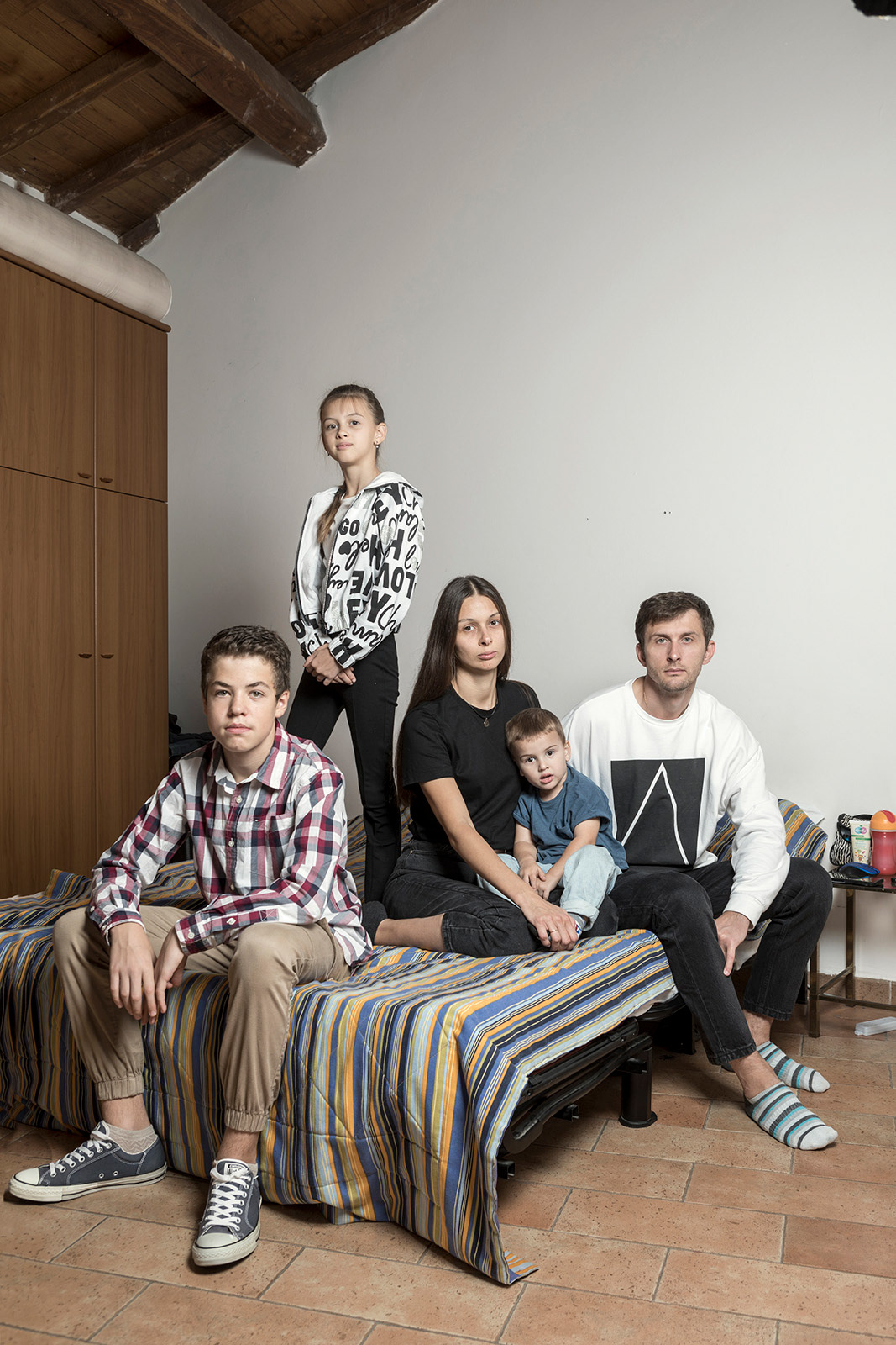 Sacrofano (Rome), Italy. 22 October 2022. The Plakhotina family, made up of Yevgen (38), Oleksandra (34) and their children Denys (14, adopted at the age of 10), Slaviana (11) and Savilii (3), in the house made available to them by the parish of Sacrofano, in the province of Rome. The family, originally from Mariupol, had lived in Odessa since 2019. Yevgen (who as a father of 3 children is exempt from martial law) works as a sailor for a Ukrainian shipping company, while Oleksandra, after her studies as a journalist, worked as a correspondent for a Mariupol station and for a magazine in Odessa. Now she takes care of the home and children full time and writes poetry. On 24 February, at the beginning of the Russian invasion, Yevgen was on board a freighter off the coast of Rotterdam, on the Netherlands, Finland and Russia routes. His phone did not pick up the signal, and he was informed of the start of the war by the second engineer on board, who, having a Dutch sim, was able to connect. Yevgen remembers initially thinking of a joke, but then when he connected through his colleague's hotspot, his phone was flooded with messages. The first thought was obviously of the family but he was unable to contact. Once in port, his phone was running regularly and he managed to get in touch with Oleksandra, who in the meantime was safely with her three children in a bunker in Odessa. Together they decided it was safer for Oleksandra and the children to leave Odessa. Oleksandra joins two other families and with three cars they head towards the border with Moldova. To get to the border, less than 100 km away, they took 18 hours, sleeping in the car. In her Oleksandra, she had also turned off the heating for fear of being suffocated by the exhaust fumes. At 8 pm they arrive at the border, and the men who drove the car had to turn back. Oleksandra and her children cross the border where they are looked after by volunteers and where they take the bus that will take them to Italy. Meanwhile, Yvgen, who was still at sea, asked to be landed in Rotterdam, two weeks before the end of the contract. He was supposed to disembark in St. Petersburg, but Yvgen refused after hearing that some members of another crew of the same company had been arrested by the Russian authorities and then reported missing. Yvgen thus lands in Poland, where he is greeted by employees of the shipping company who assist him and put him on a plane to Rome, where his family was waiting for him. The family was initially welcomed at a shelter and prayer center near Sacrofano, in the province of Rome, and then moved to a hotel in Pomezia, where they stayed two months waiting for a priest's house to be ready. of the Parish of Sacrofano where they still stay. Denys is attending the last year of middle school online and plays basketball for a team in Sacrofano. Slaviana is attending the last year of elementary school both on presence in an italian school and on line with her school in Odessa, and she also continues her violin lessons online. Since returning, Yvgen has also worked a shift at sea between the Netherlands, England and Spain. Only Yvgen's parents are left in Mariupol, who are retired and have decided to stay in their home. The father, even after retiring, provided consultancy at the Azovstal factory, where he worked.