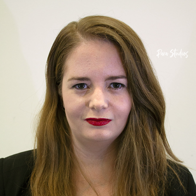 A portrait of Jennifer, they wear a black jacket and red lipstick.