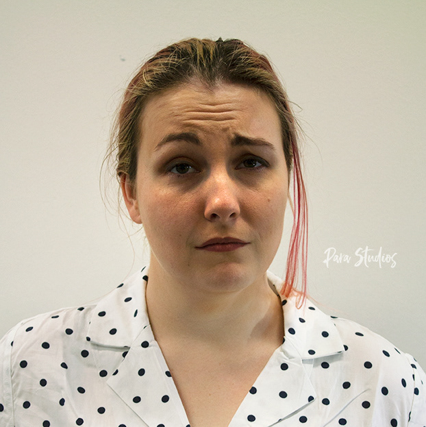 A portrait of Angela, they wear their hair in a ponytail and a white blouse with black polkadots.