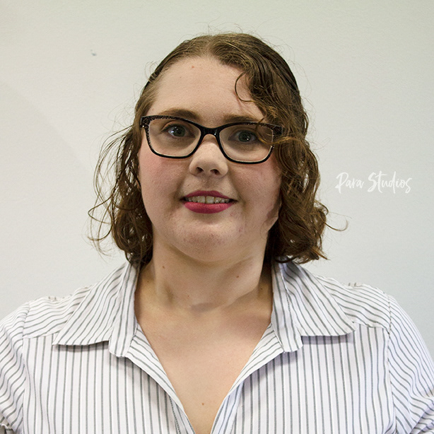 A portrait of Lana, they wear a striped white blouse and glasses.