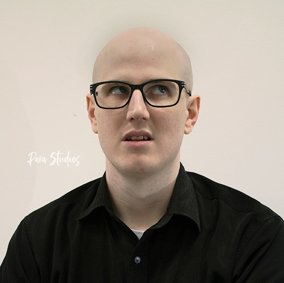 A portrait of Devon, they wear a black shirt and glasses.)