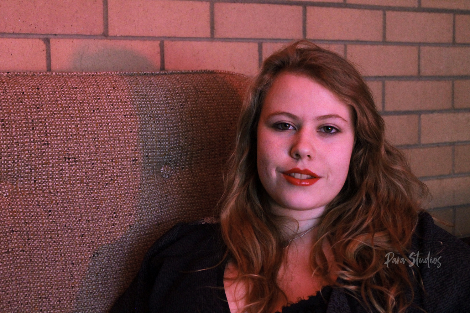 "Relaxed". A woman sits on a couch wearing red lipstick.