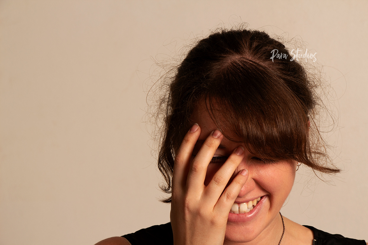 "Tickled". A woman sits laughing, covering half of her face with her hand.