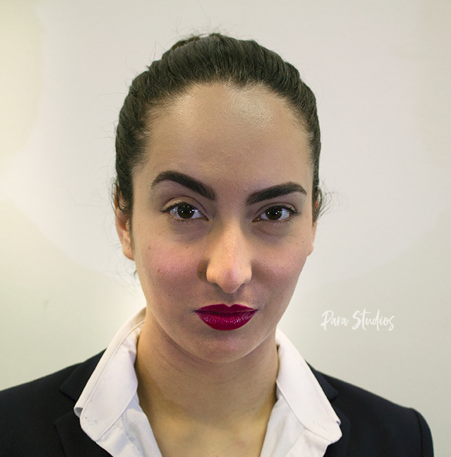 A portrait of Sharon, they wear a white blouse, black jacket and their hair tied back.