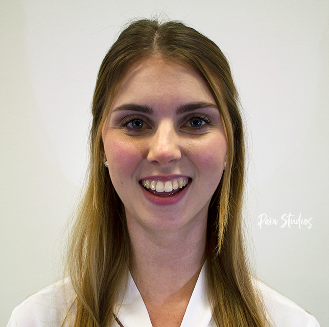 A portrait of Tracy, they wear a white blouse and their hair half up/half down.