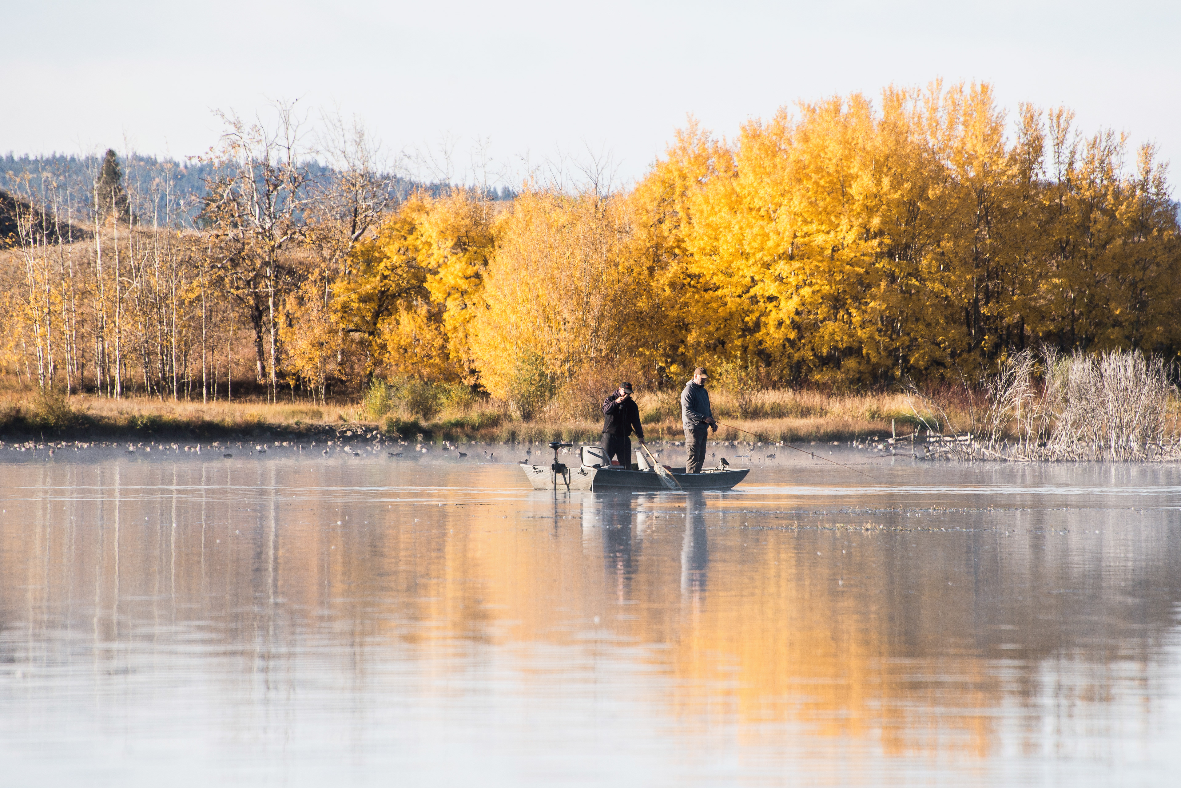 two flyfishers in a boat on Stoney Lake, BC, with colourful fall foliage on the shoreline in the background