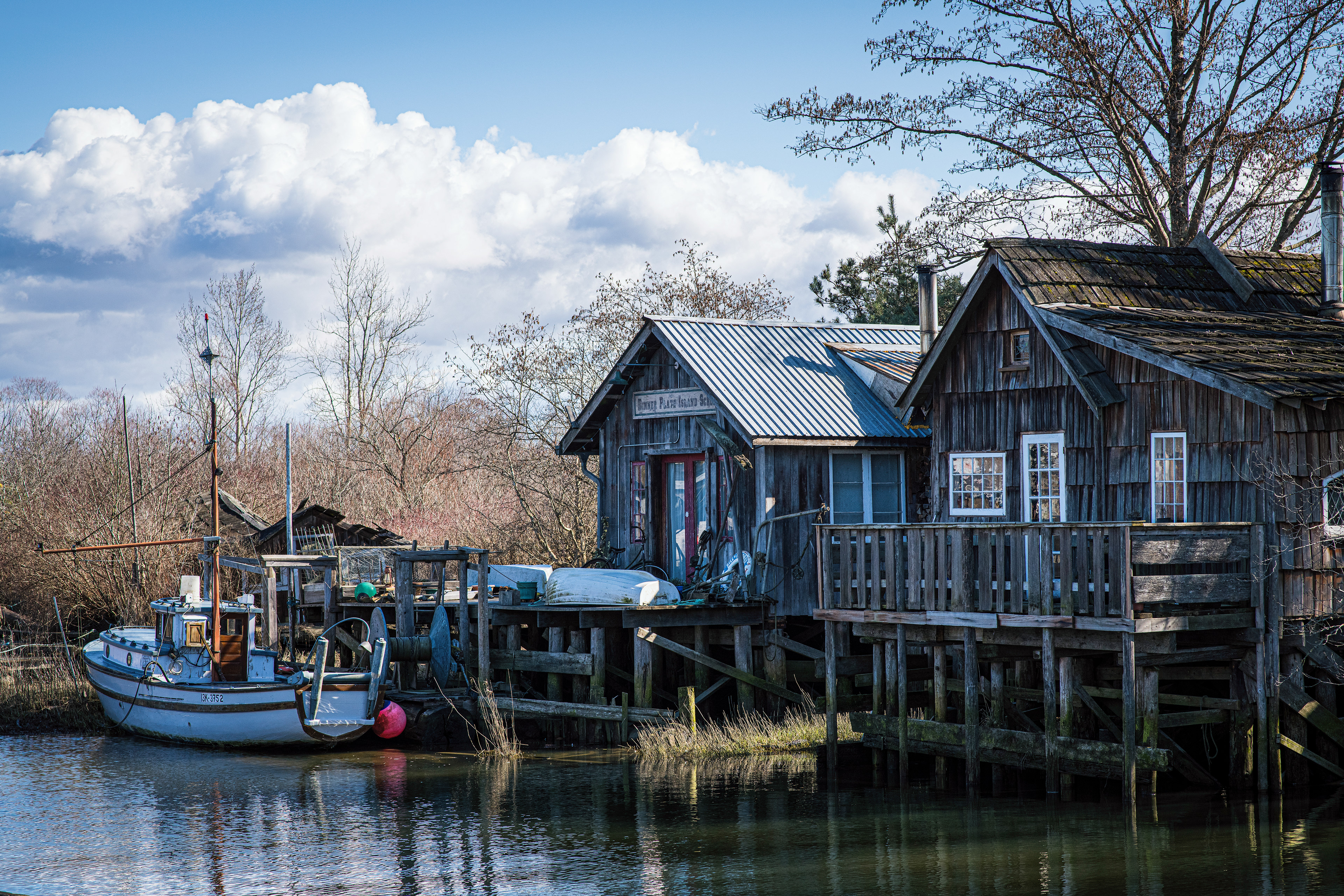 Old small wooden gill netter fish boat moored alongside shingled homes in Finn Slough, Richmond, BC