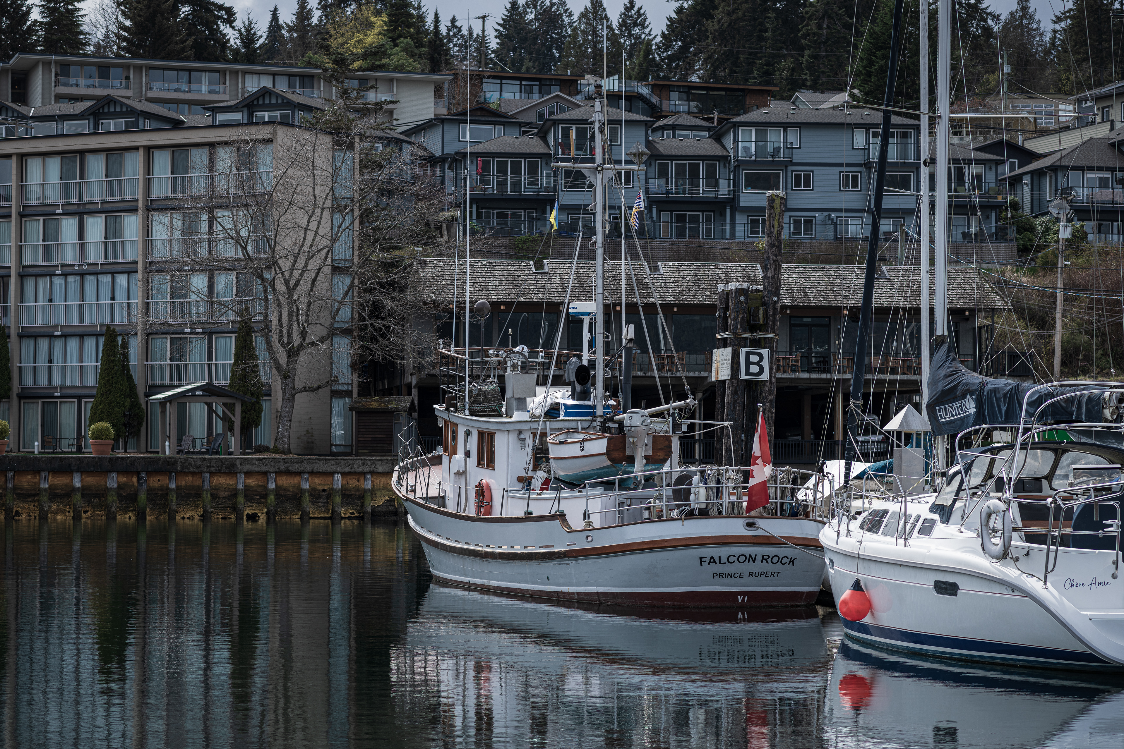 two yachts moored in calm reflecting waters at Cowichan Bay, BC, with apartment buildings in the background