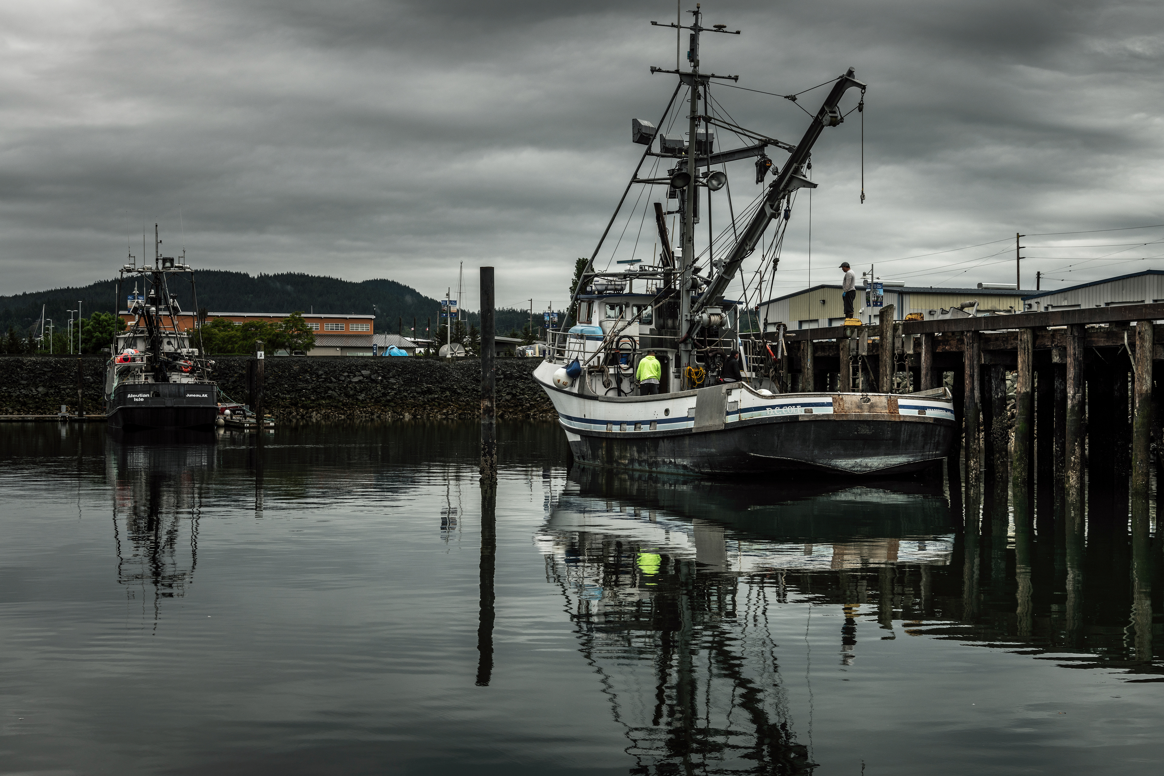 Lareg commercial fish boat moored in calm waters at Anacortes WA, with ship reflections in the foreground and dark clouds in the background