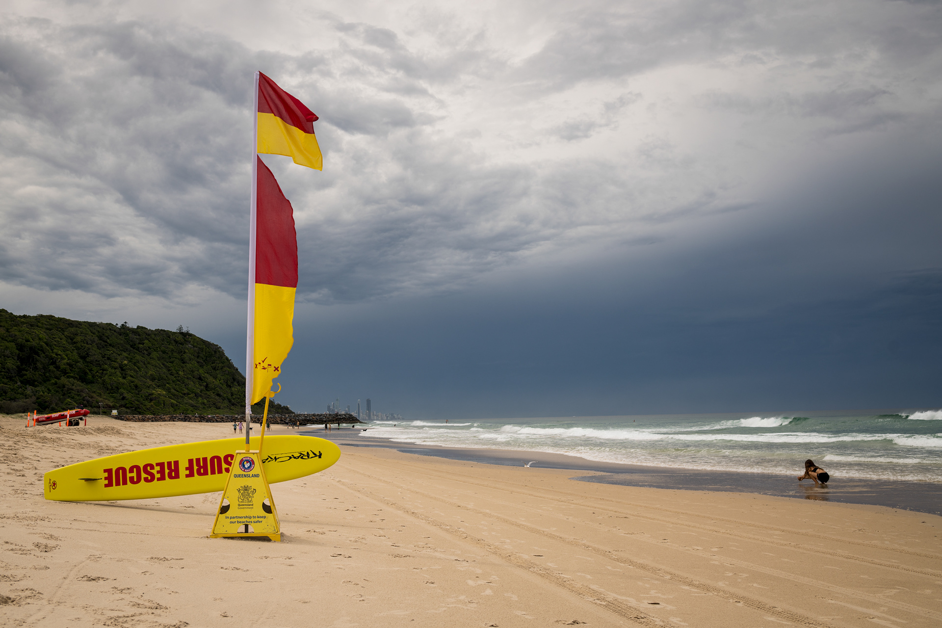 Red and yellow surf lifesaving flags on a sandy beach on the Gold Coast, Queensland, with surf and dark cloudy sky in the background