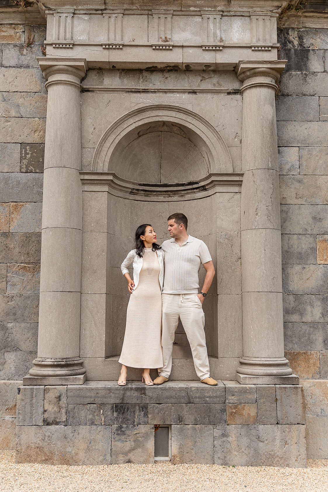 Wedding couple hold each and look at each other in a stone pillar alcove