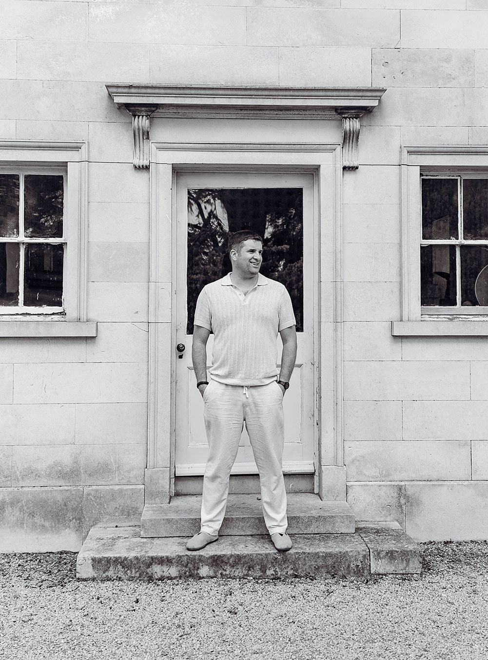 Groom standing in front of door of stone building looking off camera