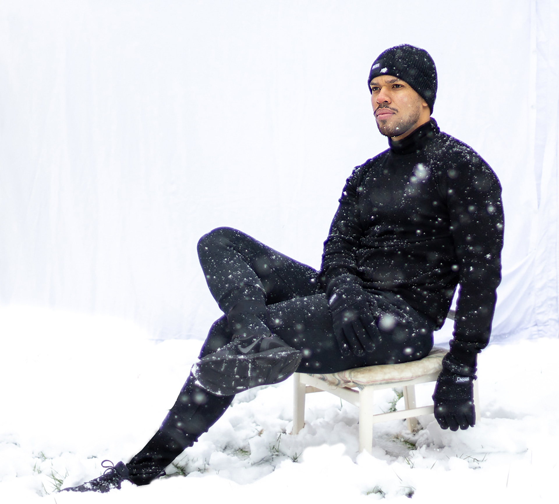 Man wearing all black sits outside in the snow against white backdrop