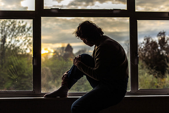 person sitting in window frame looking out at dusk