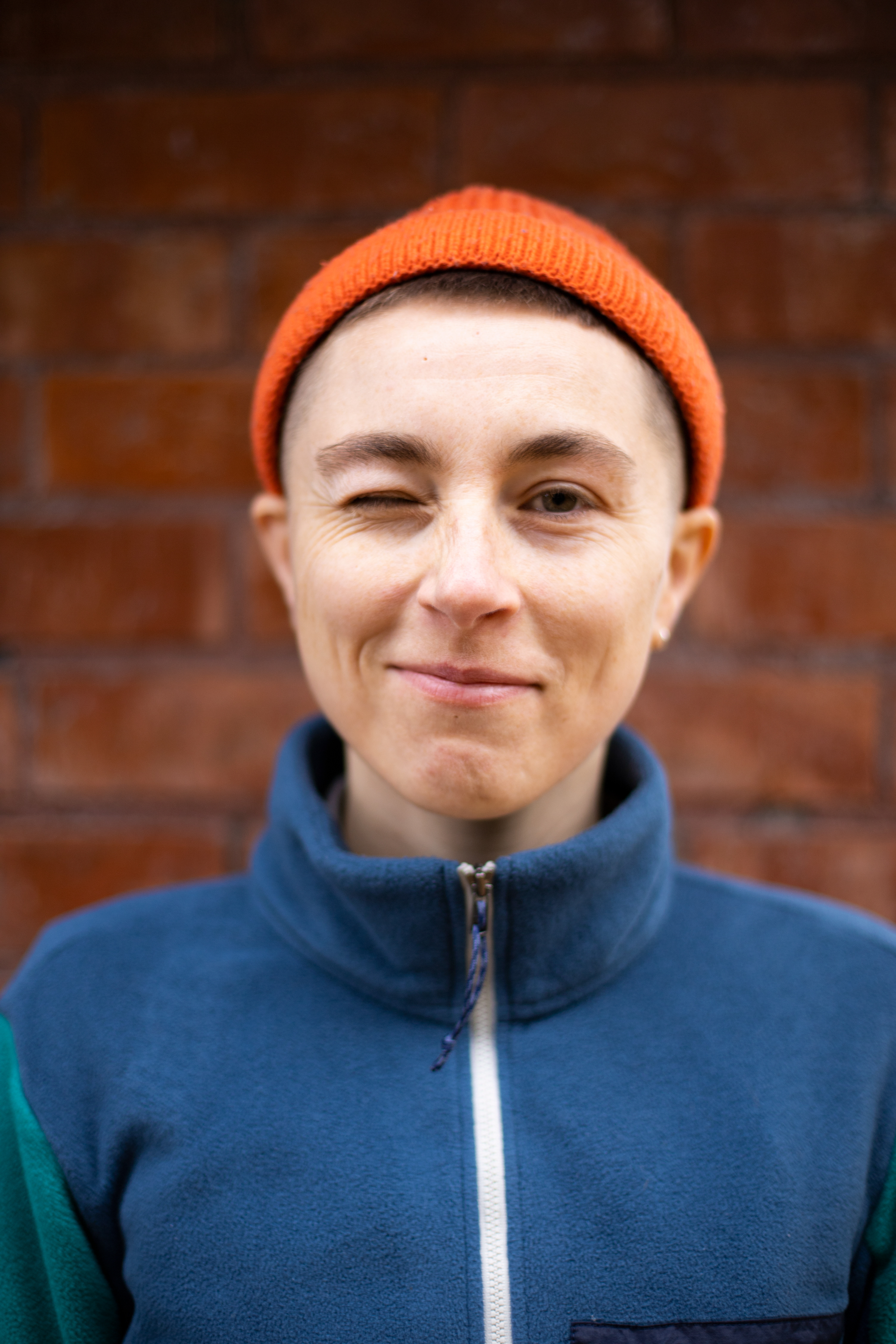 close up portrait of person in orange hat and blue fleece winking and smiling
