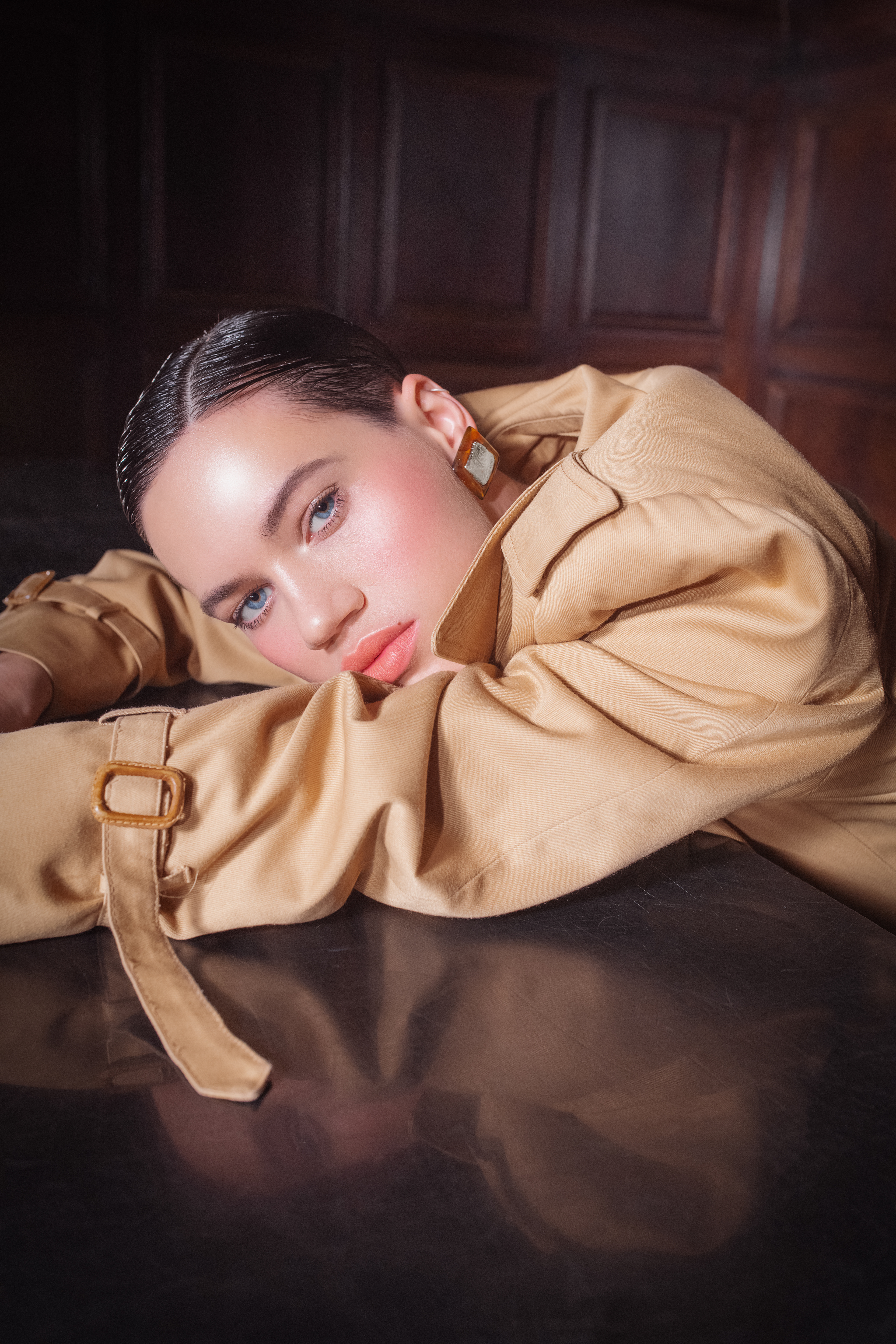 beauty shot of a woman with blue eyes, pink lip gloss. She's wearing a long brown trenchcoat with brown and silver earrings