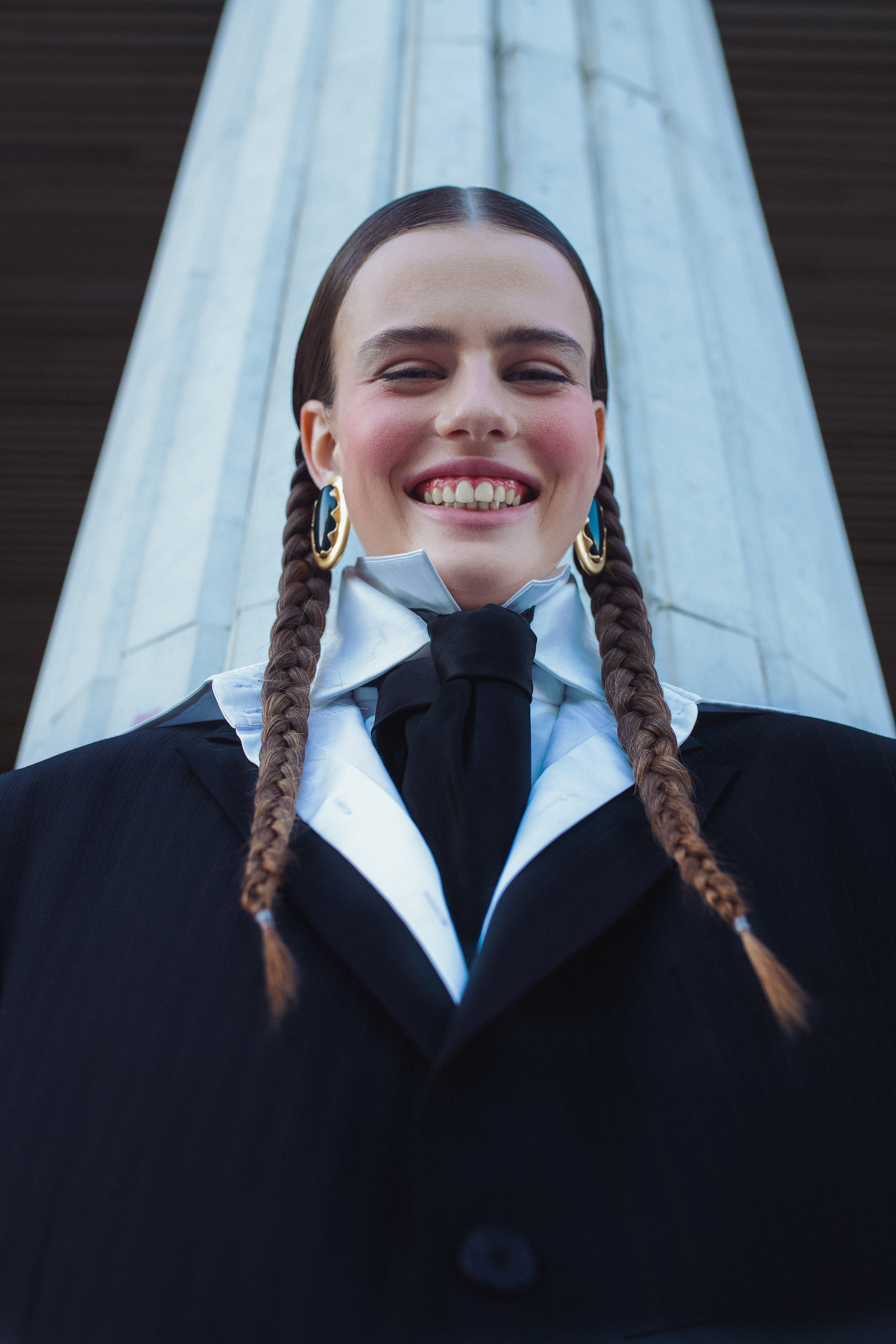 smiling woman in a tuxedo with black and white. gold earrings. 