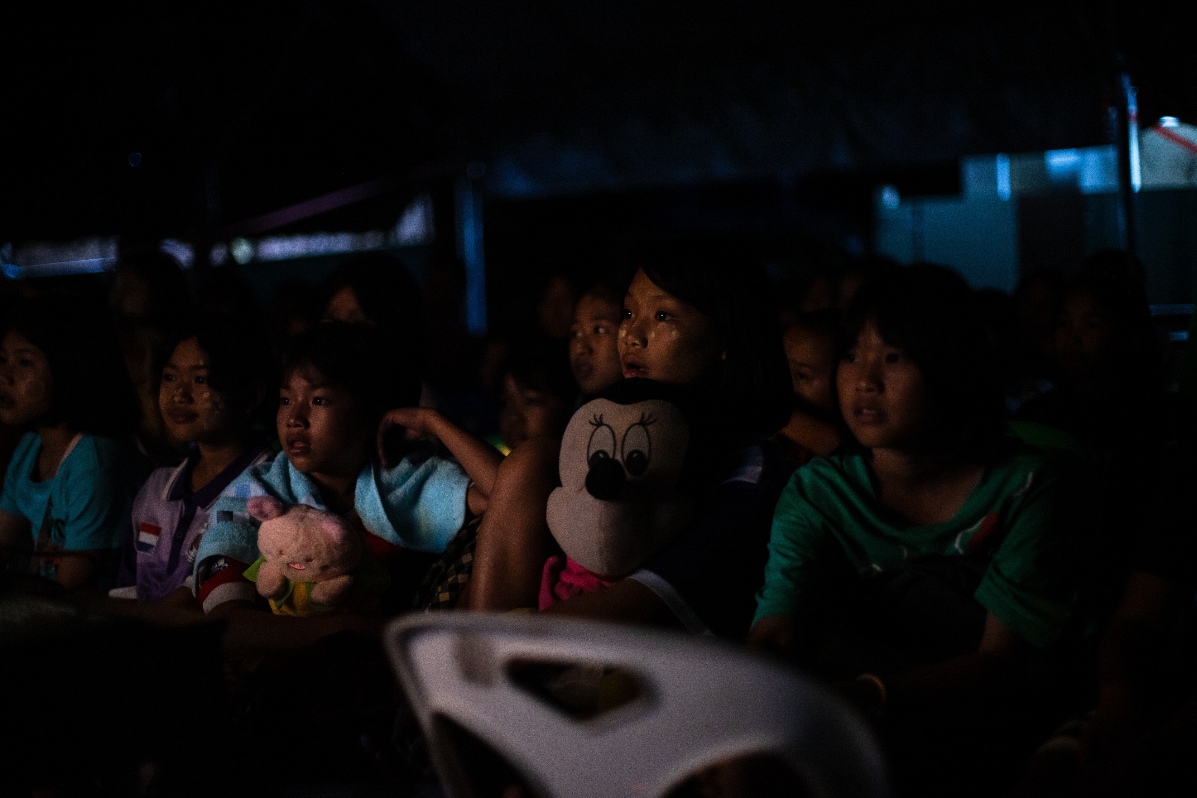 Students gather in the dormitory at night to watch a film together during summer camp at KKB School. The movie is projected onto a wall, thanks to a setup provided by one of the camp’s volunteers. July 2024