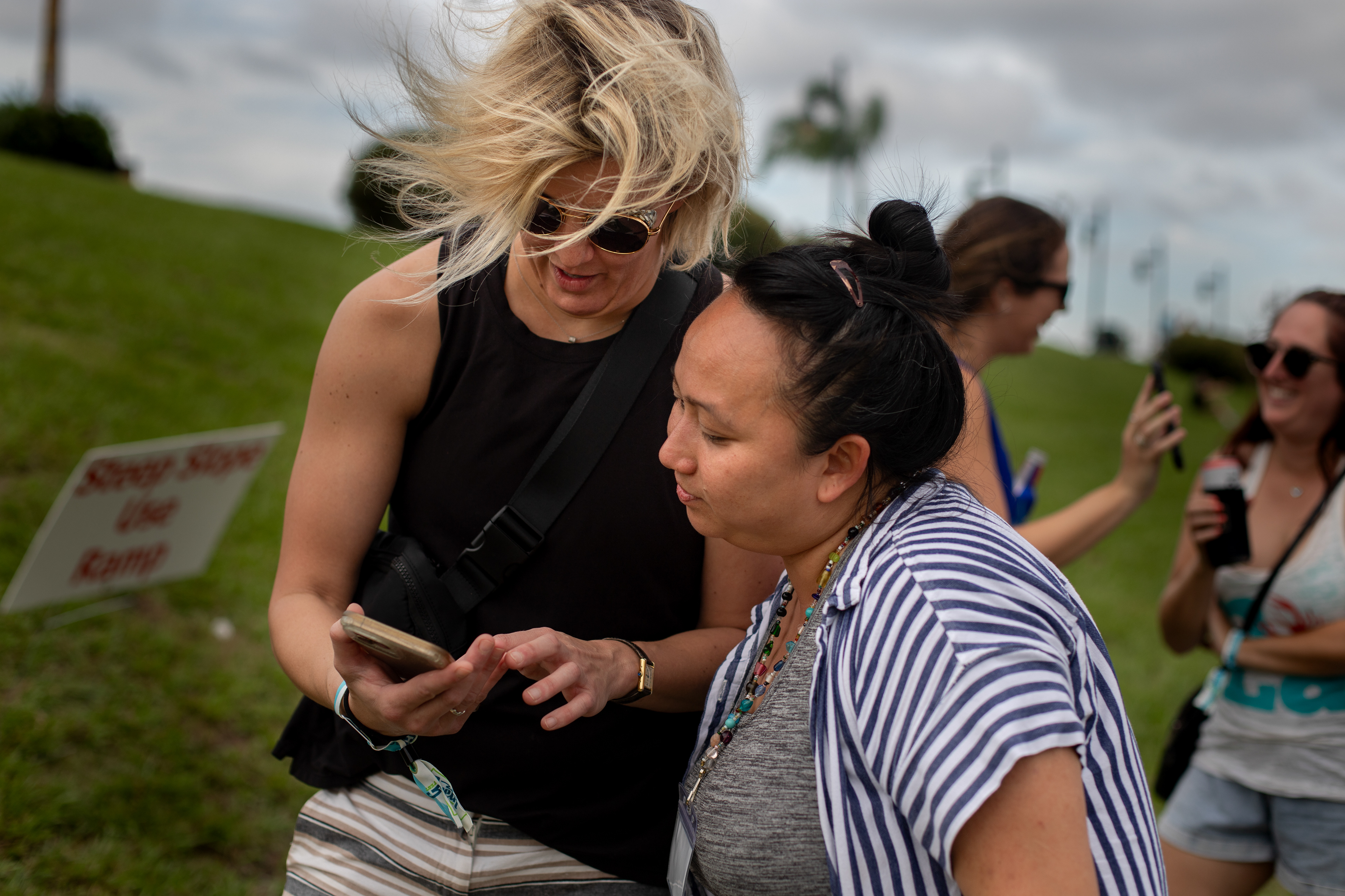 Anh Luu reconnects with a middle school friend Caitlin after many years at the Gretna festival where she is helping run a gelato stall with her friend. Her friend shows her photos of her children on her phone.