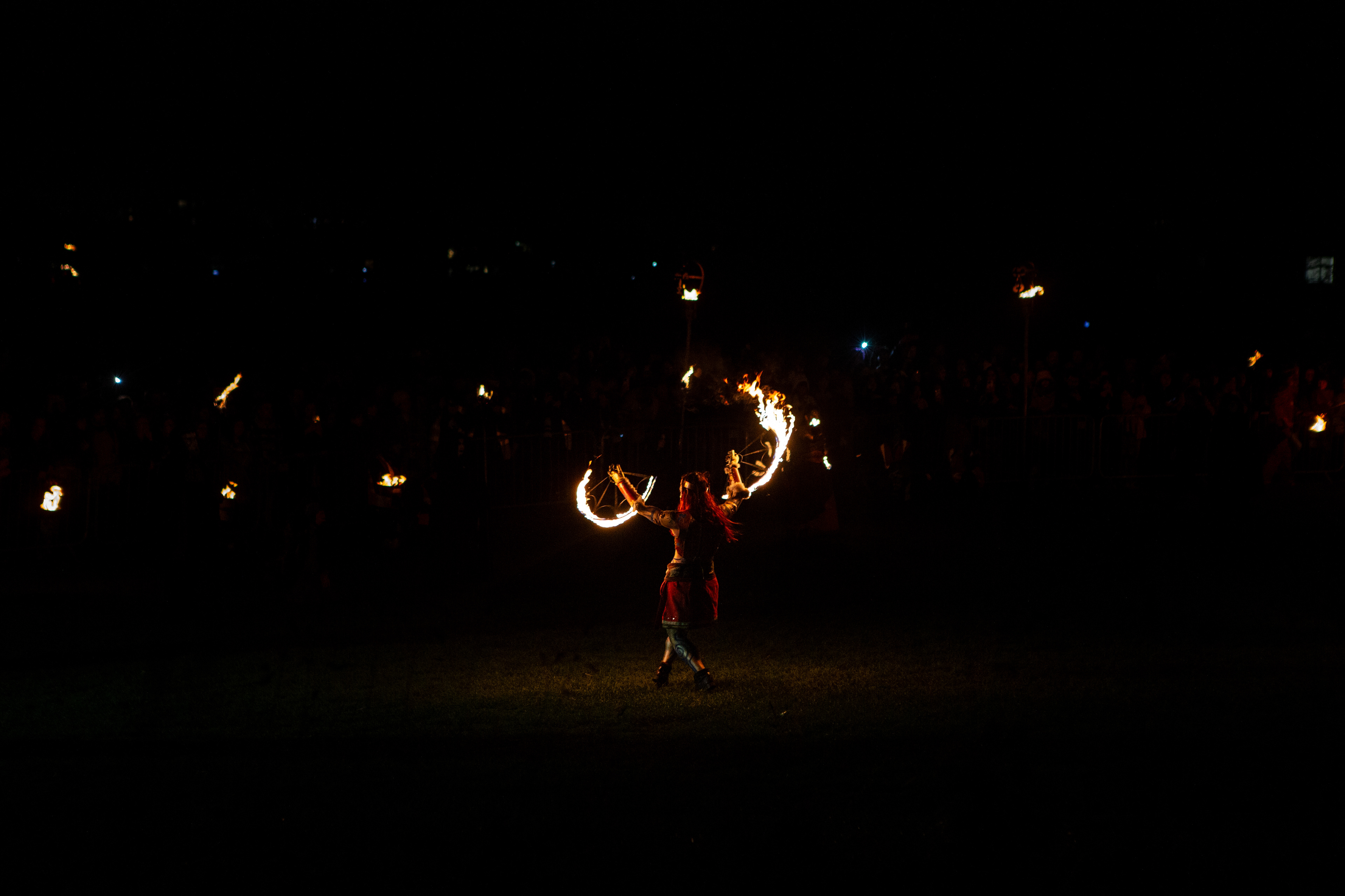 A performer performs with fire at the festival. The festival goers are protected by a fence, ensuring they are far enough from the performers.