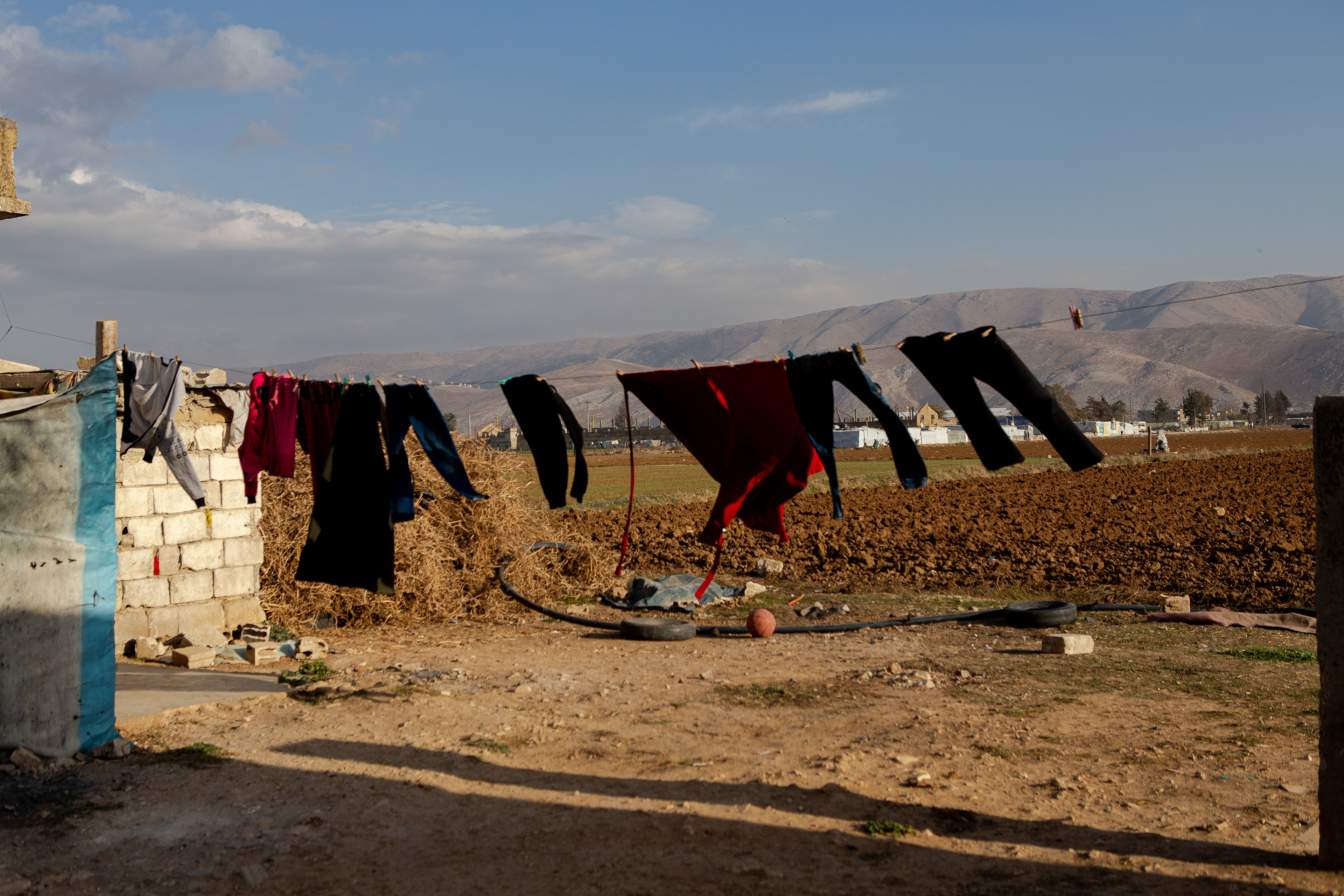 Maryam's children's clothes hang on a makeshift clothesline beside her tented home on the land she cultivates. With no crops to harvest this winter season, she works on her neighbors' fields in the Bekaa Valley to support her family.