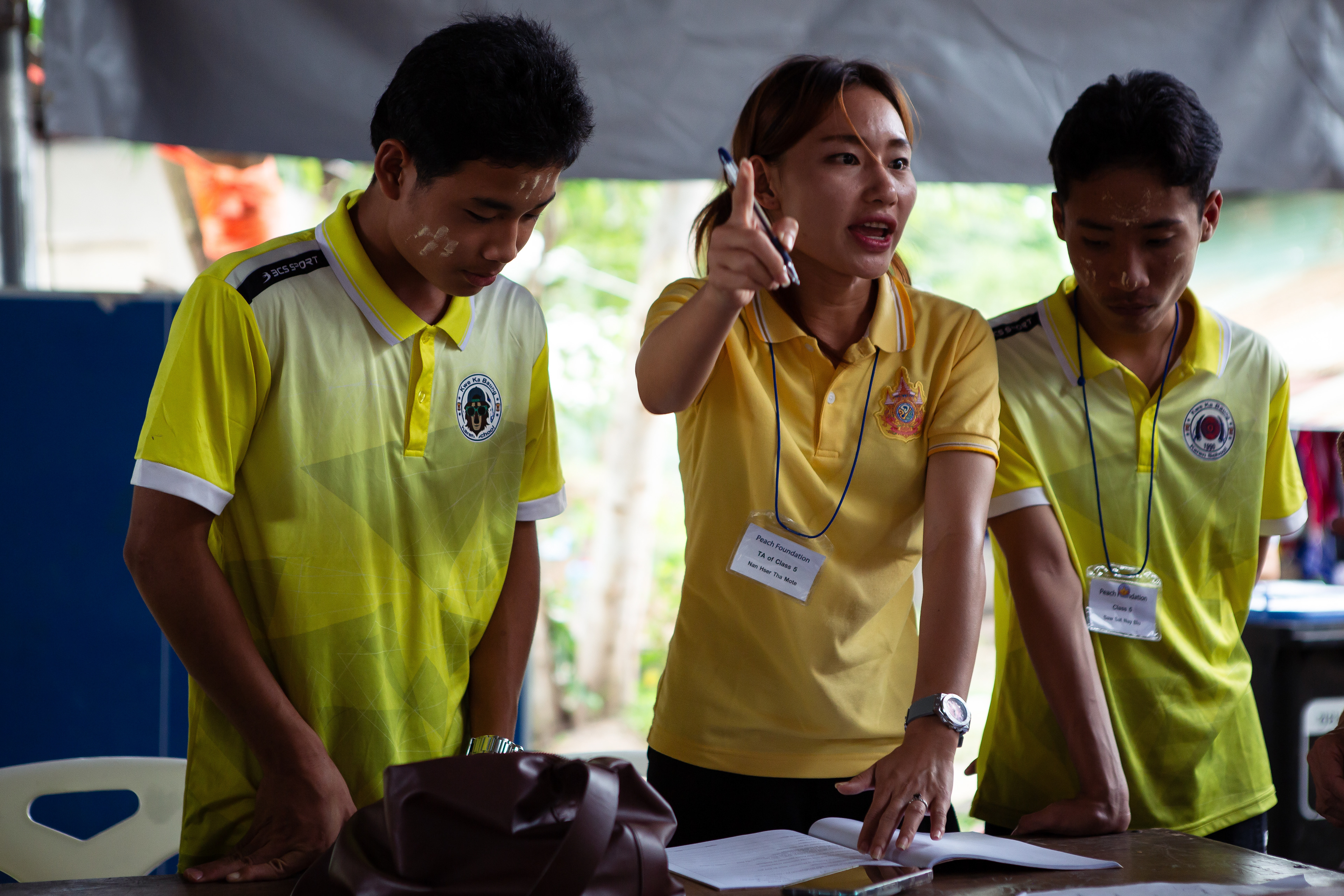 Nan Hser Tha Mote gently disciplines students while marking their homework. She is refugee from Myanmar educated in Thailand and now teaches the next generation of displaced children. July 2024