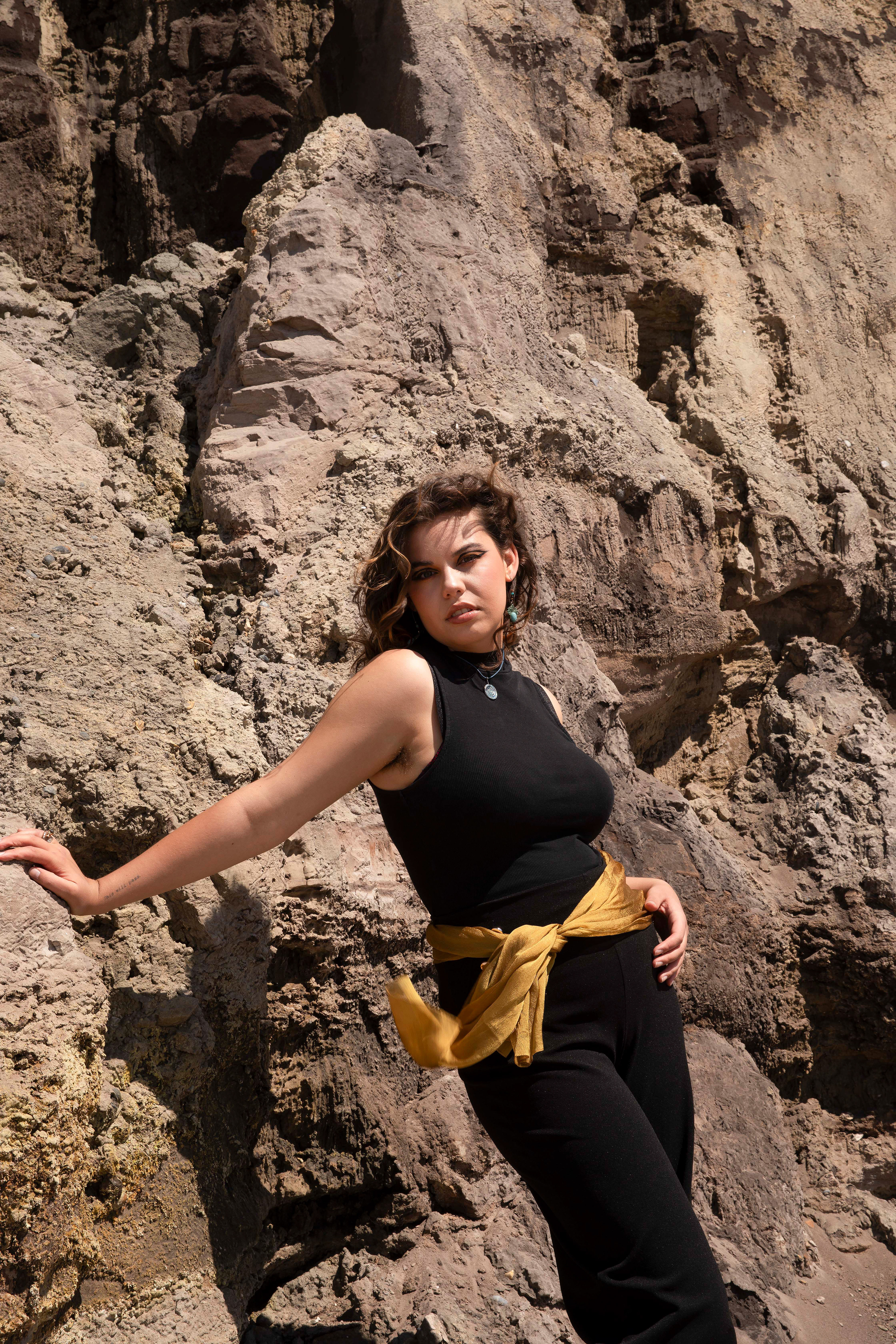 a person leaning against some rocks in a black outfit with a gold sash