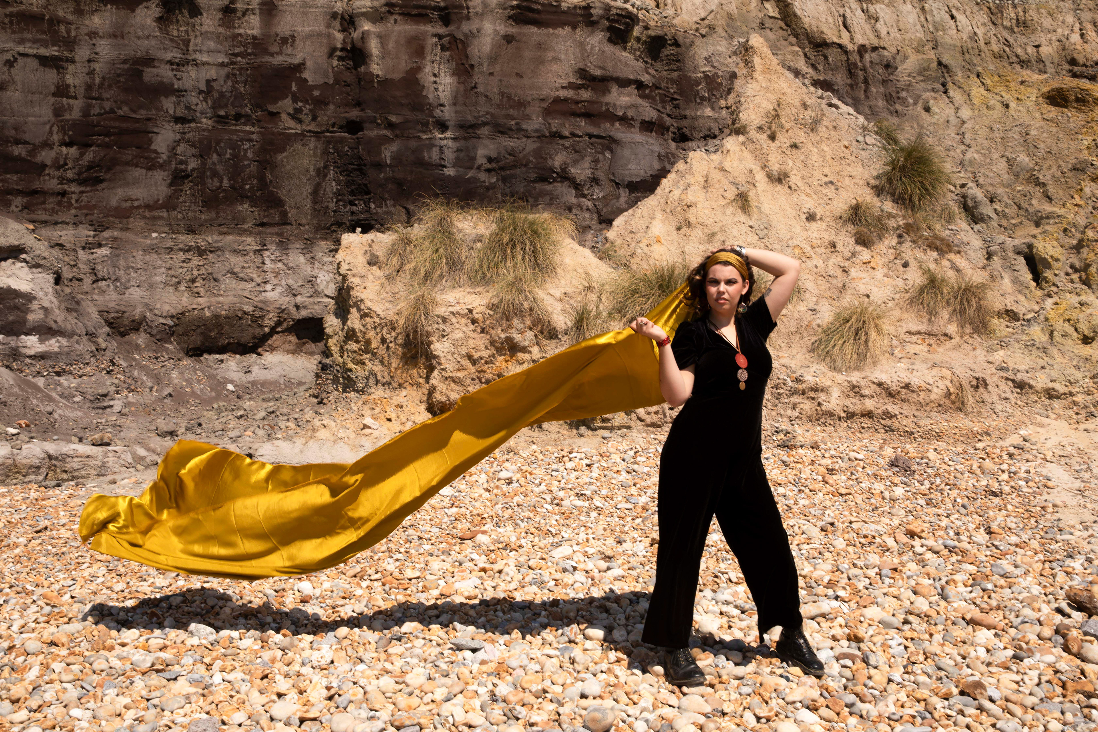 A person stood in front of cliffs with floating gold fabric behind them