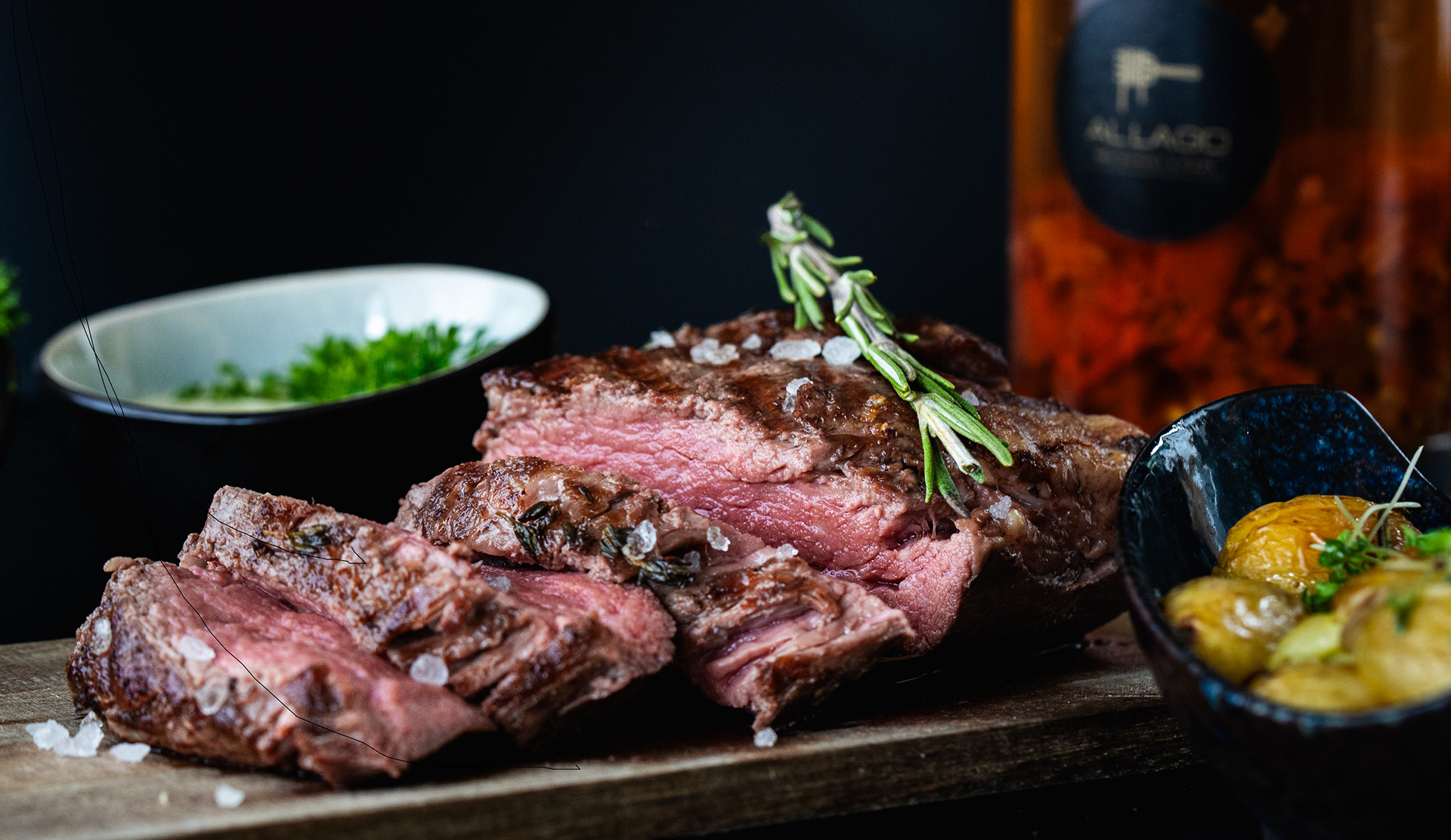 Medium gebratenes Steak mit Kräutern und Beilagen – stimmungsvolle, kontrastreiche Foodfotografie im dunklen Stil.