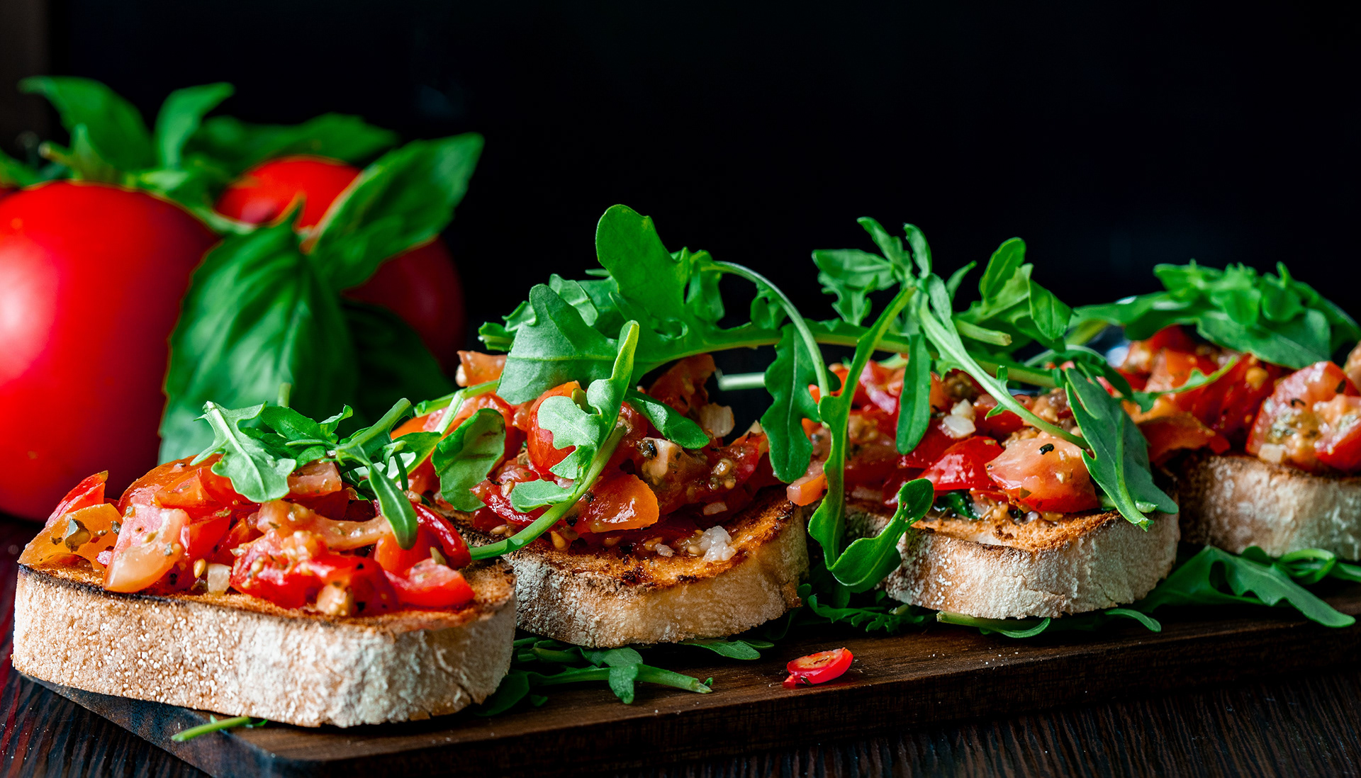 Bruschetta im Detail, Nahaufnahme mit frischen Tomaten, Basilikum und Rucola.