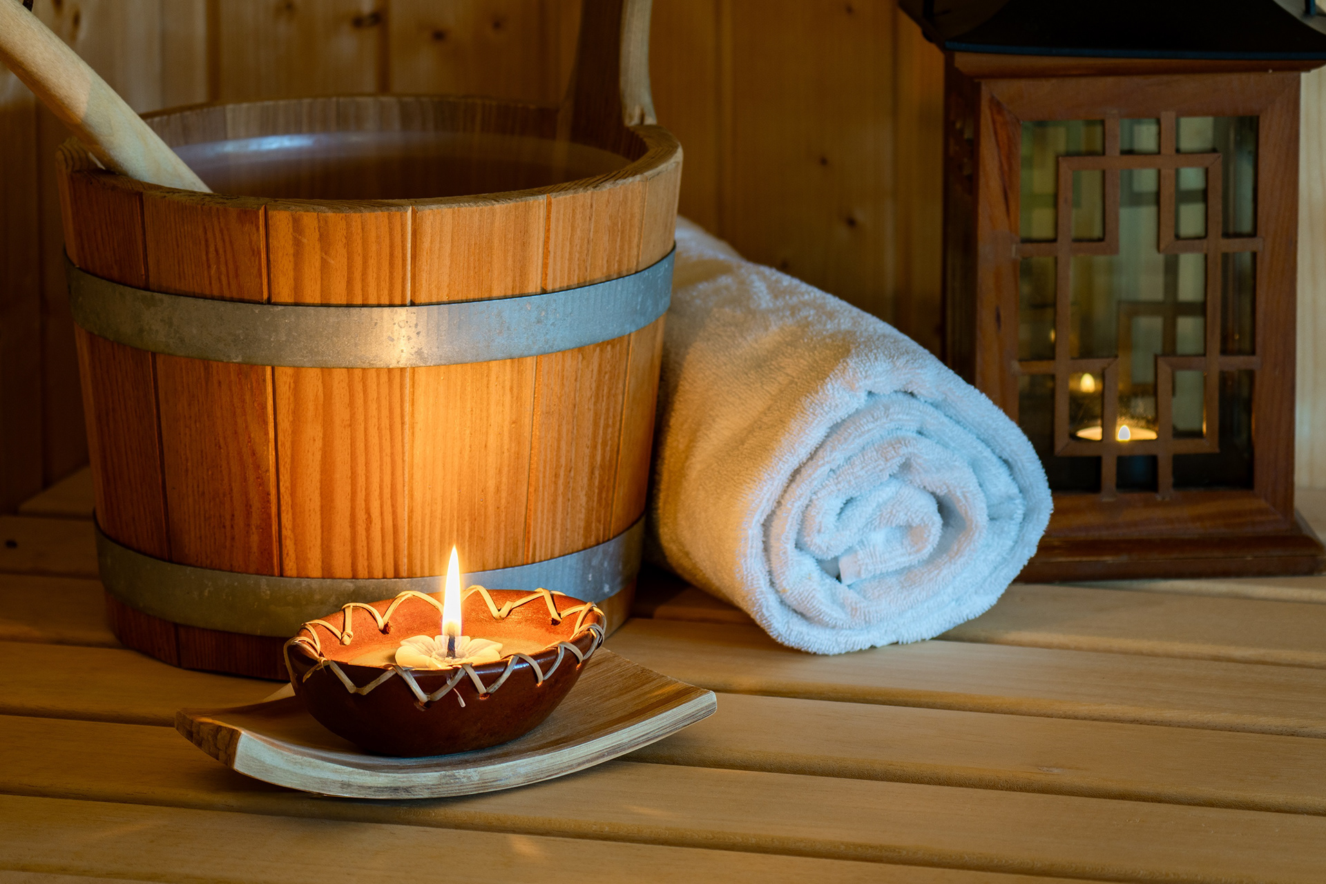 Interiorfotografie Sauna mit Handtuch, Holzeimer und Kerze – warme Wellness-Atmosphäre.