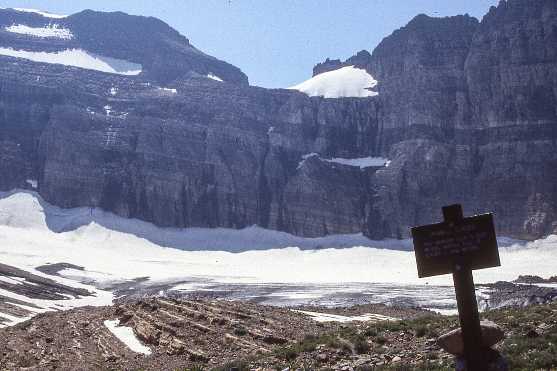The sign reads:GRINNELL GLACIERTHIS OVERLOOK ELEV. IS 2000METERS. AVERAGE ELEV OFGLACIER IS 2046 METERS.