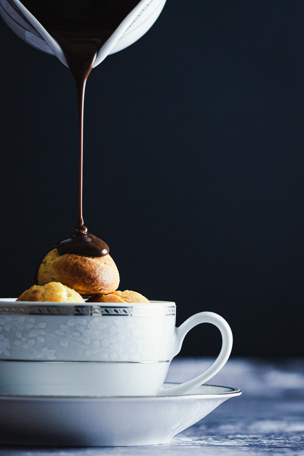 Chocolate sauce poured over profiteroles in a teacup