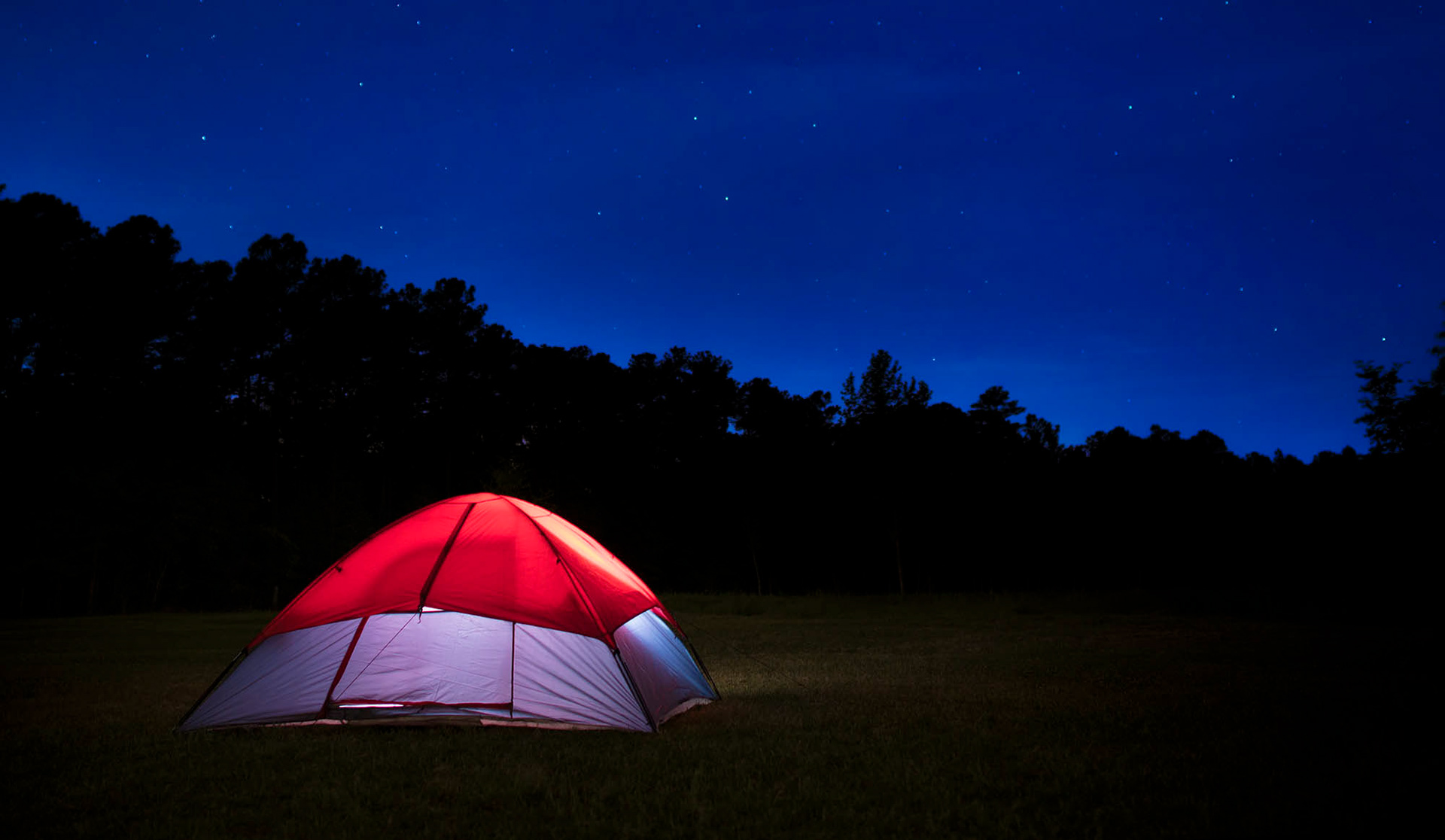 Lighted dome tent at night with stars shining above by Guy Sagi